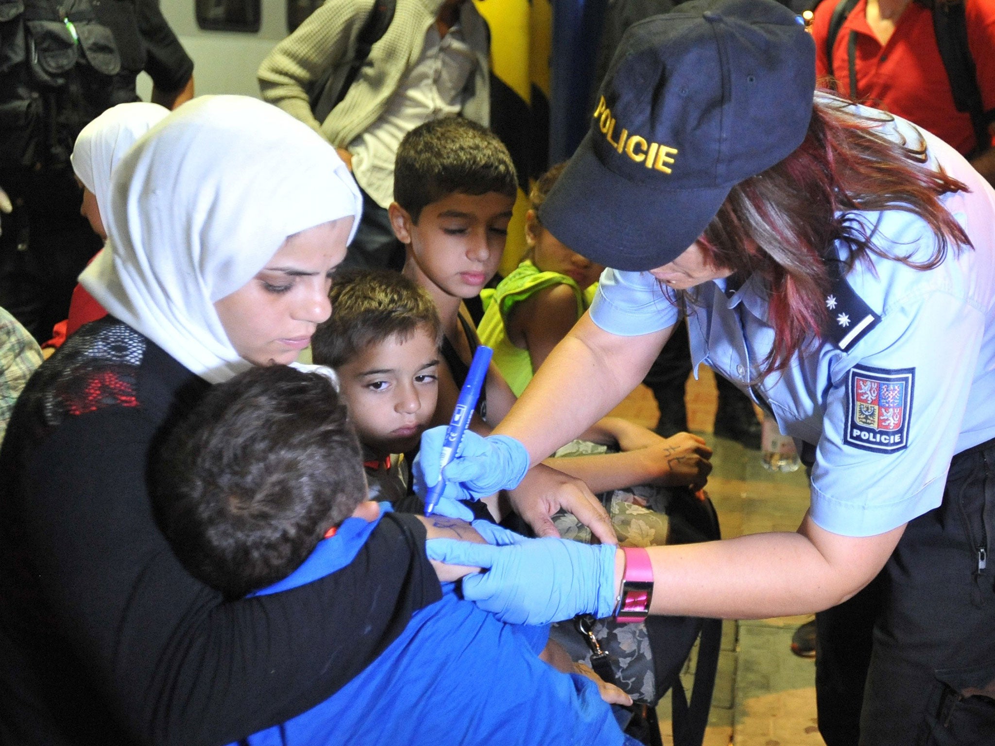 A Czech police officer marks a refugee with a number after more than than 200 refugees were detained on trains from Hungary and Austria