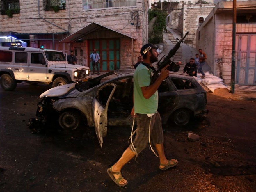 An Israeli settler walks past a burned out vehicle used by US tourists after it was attacked by Palestinians in the West Bank city of Hebron, 03 September 2015.