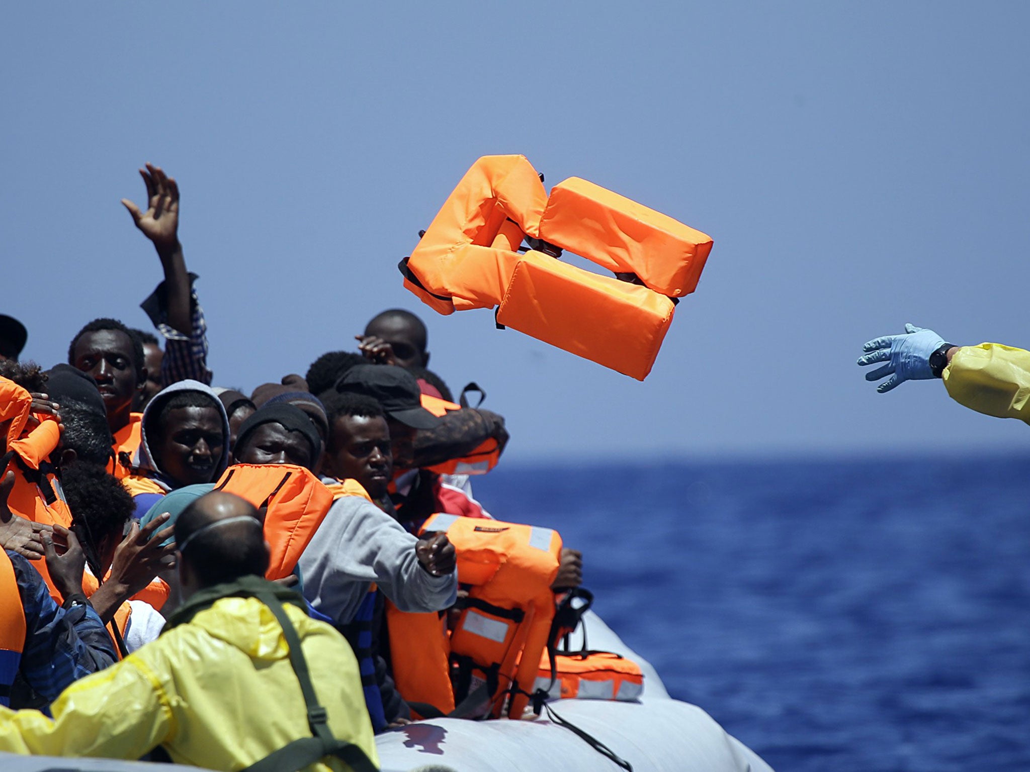 A Belgian navy sailor tosses a life vest to migrants sitting in a rubber boat as they approach the Belgian Navy Vessel Godetia during a search and rescue mission in the Mediterranean Sea off the Libyan coast in June