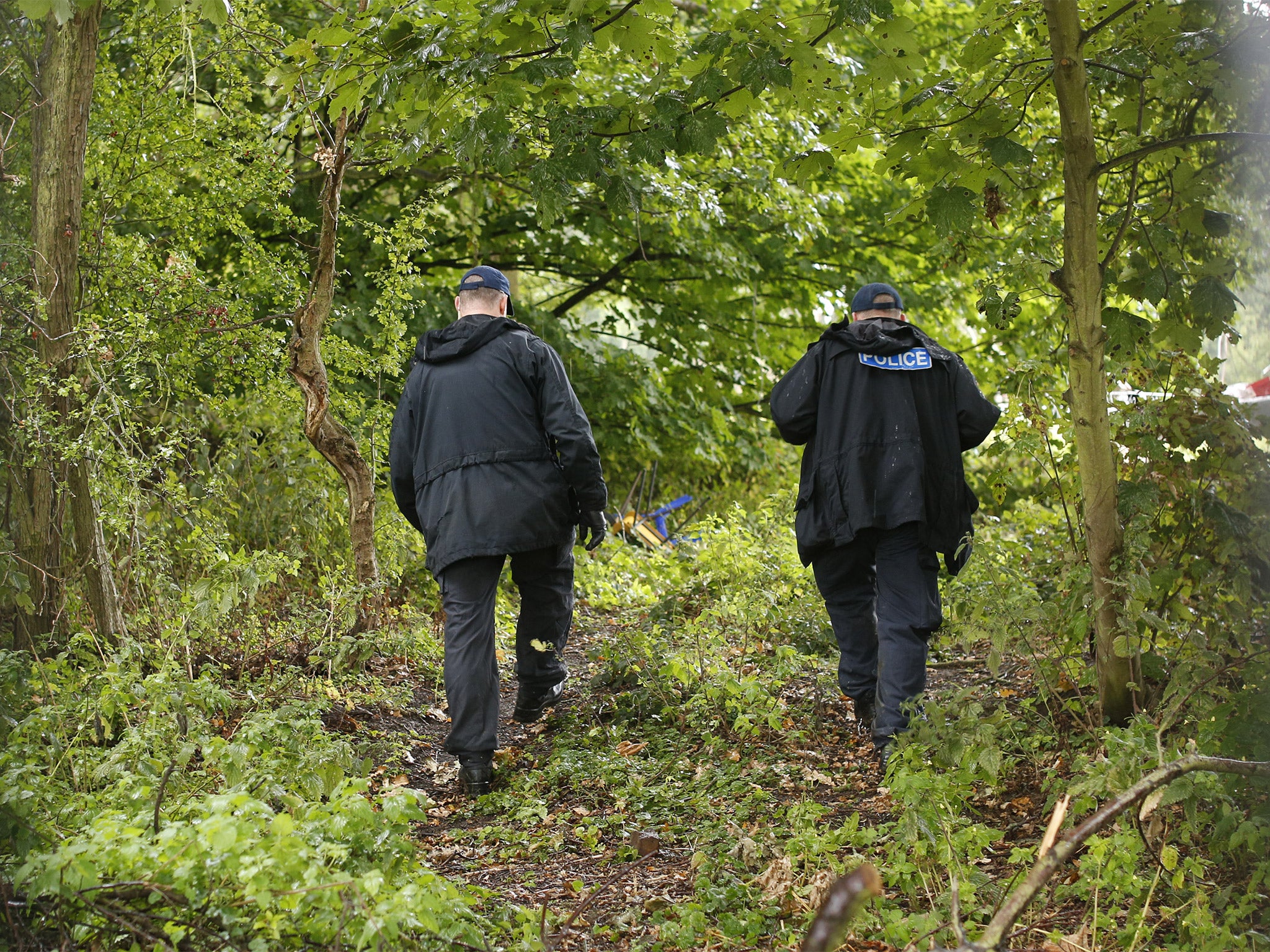 Police officers walk through the forest in Runnymede