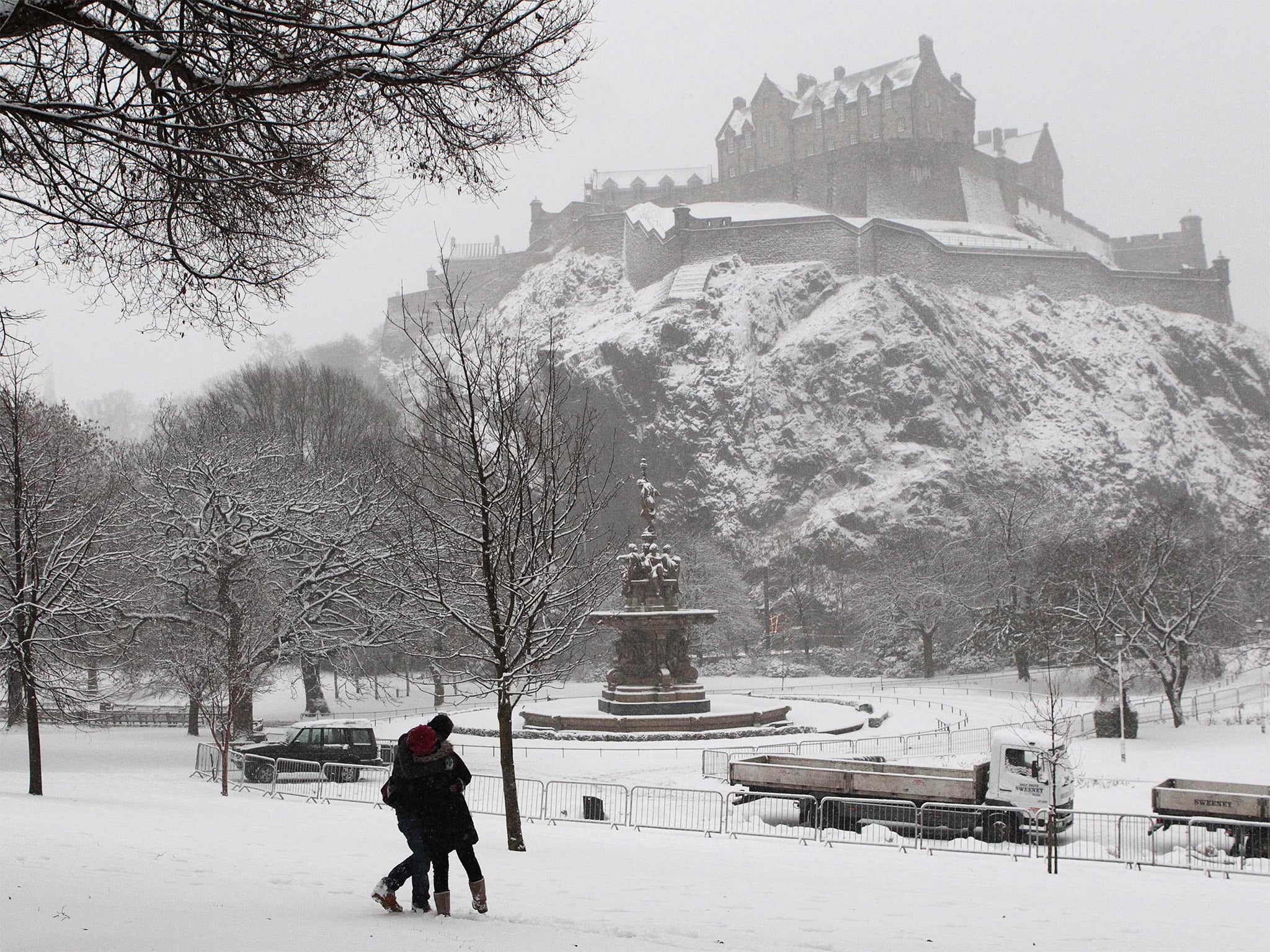 A couple embrace as they stand in snow below Edinburgh castle