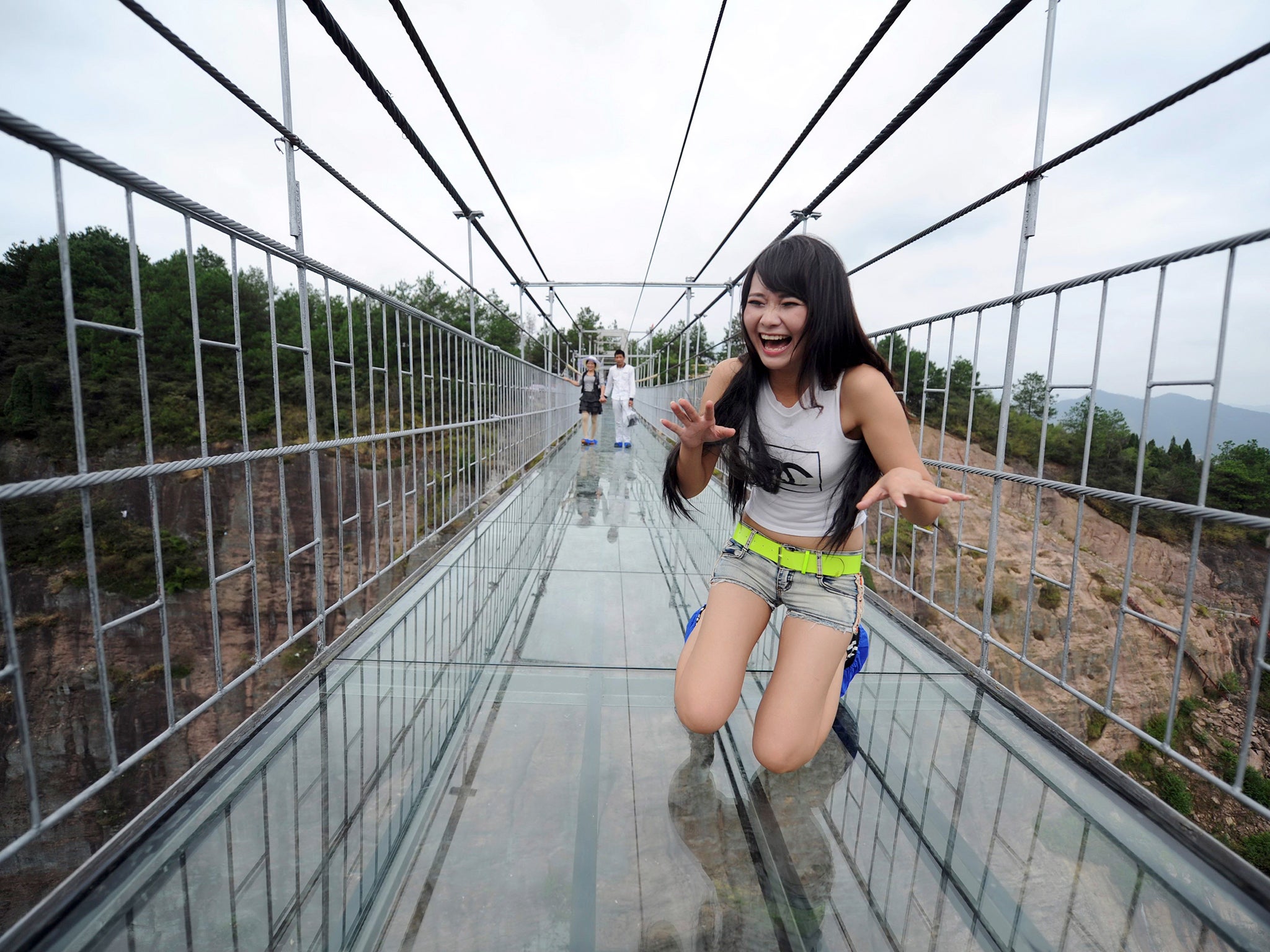 A woman plays around as she walks across a glass-bottomed suspension bridge in a scenic zone in Pingjiang county in southern China's Hunan province