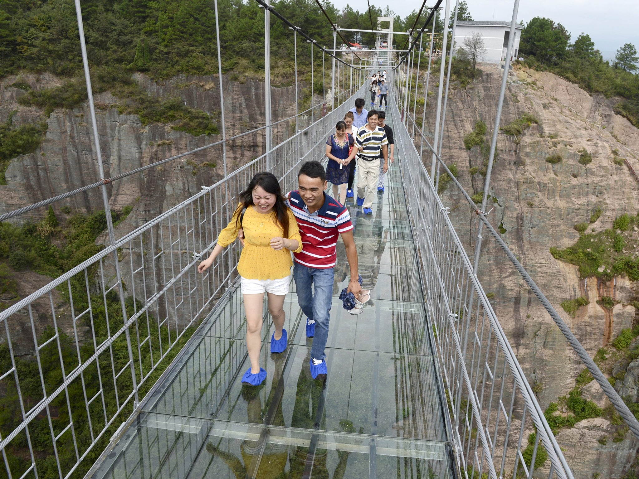 Tourists walk on a glass suspension bridge at the Shiniuzhai National Geo-park in Pinging county, Hunan province, China