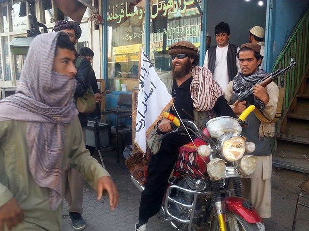 A Taliban fighter sits on a motorcycle adorned with a Taliban flag in Kunduz, Afghanistan