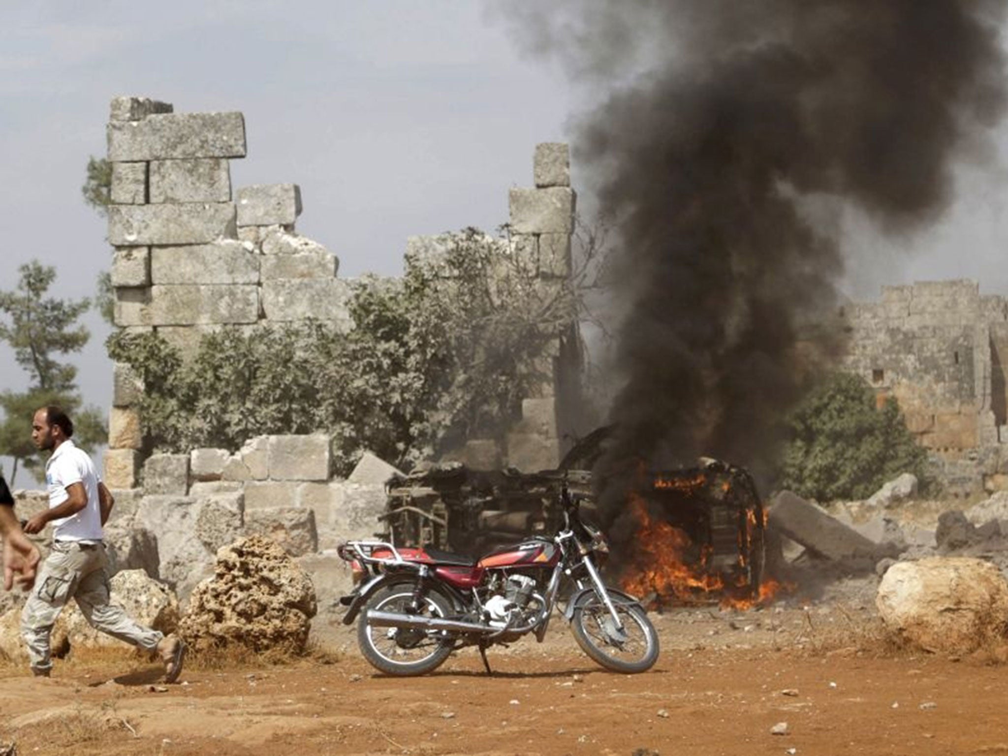 A man runs past a burning military vehicle at a base controlled by rebel fighters from the Ahrar al-Sham Movement, that was targeted by what activists said were Russian airstrikes at Hass ancient cemeteries in the southern countryside of Idlib, Syria