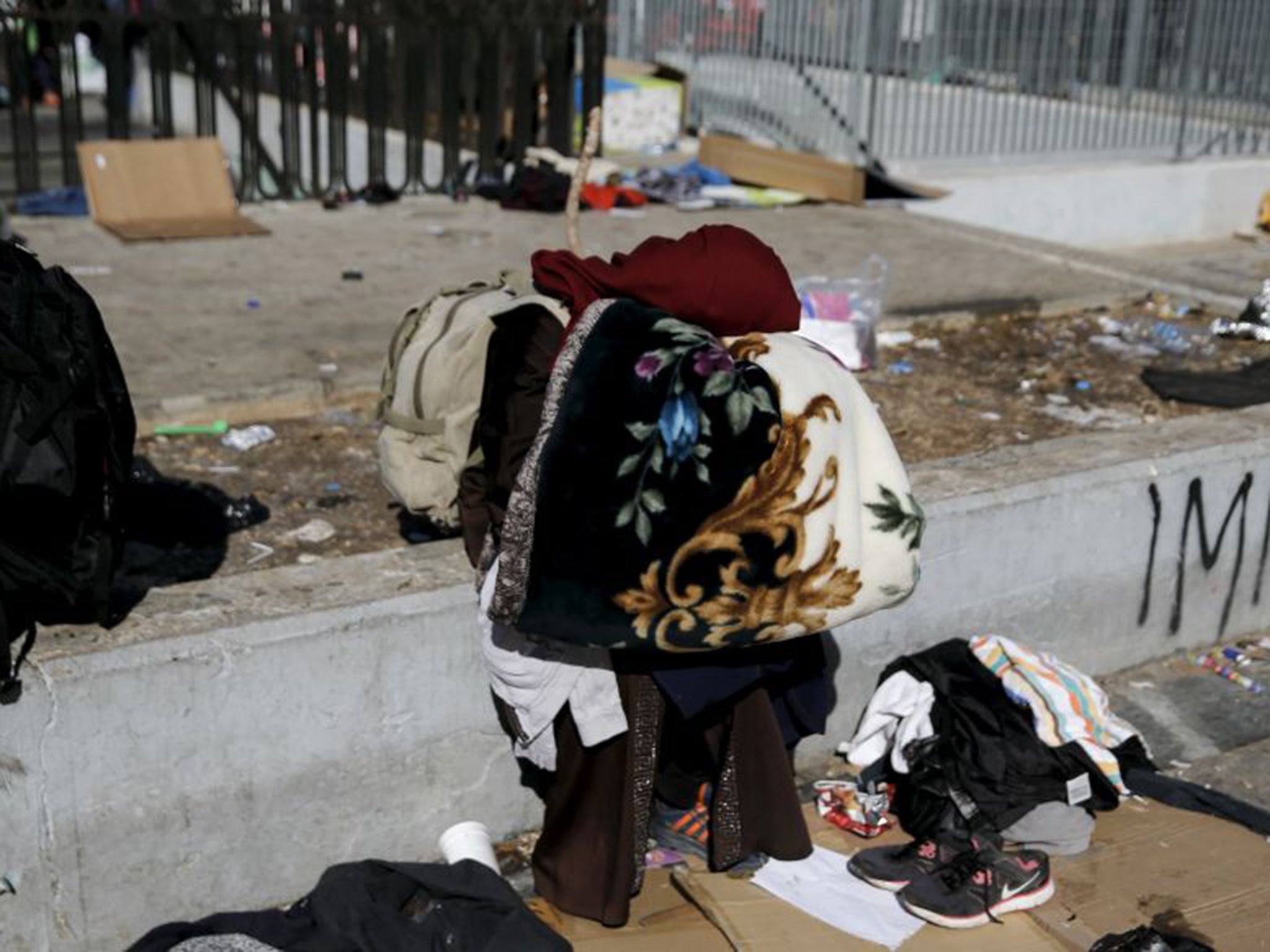 An Afghan refugee holds some blankets as refugees wait to be transferred from Victoria Square to one the stadiums in Athens