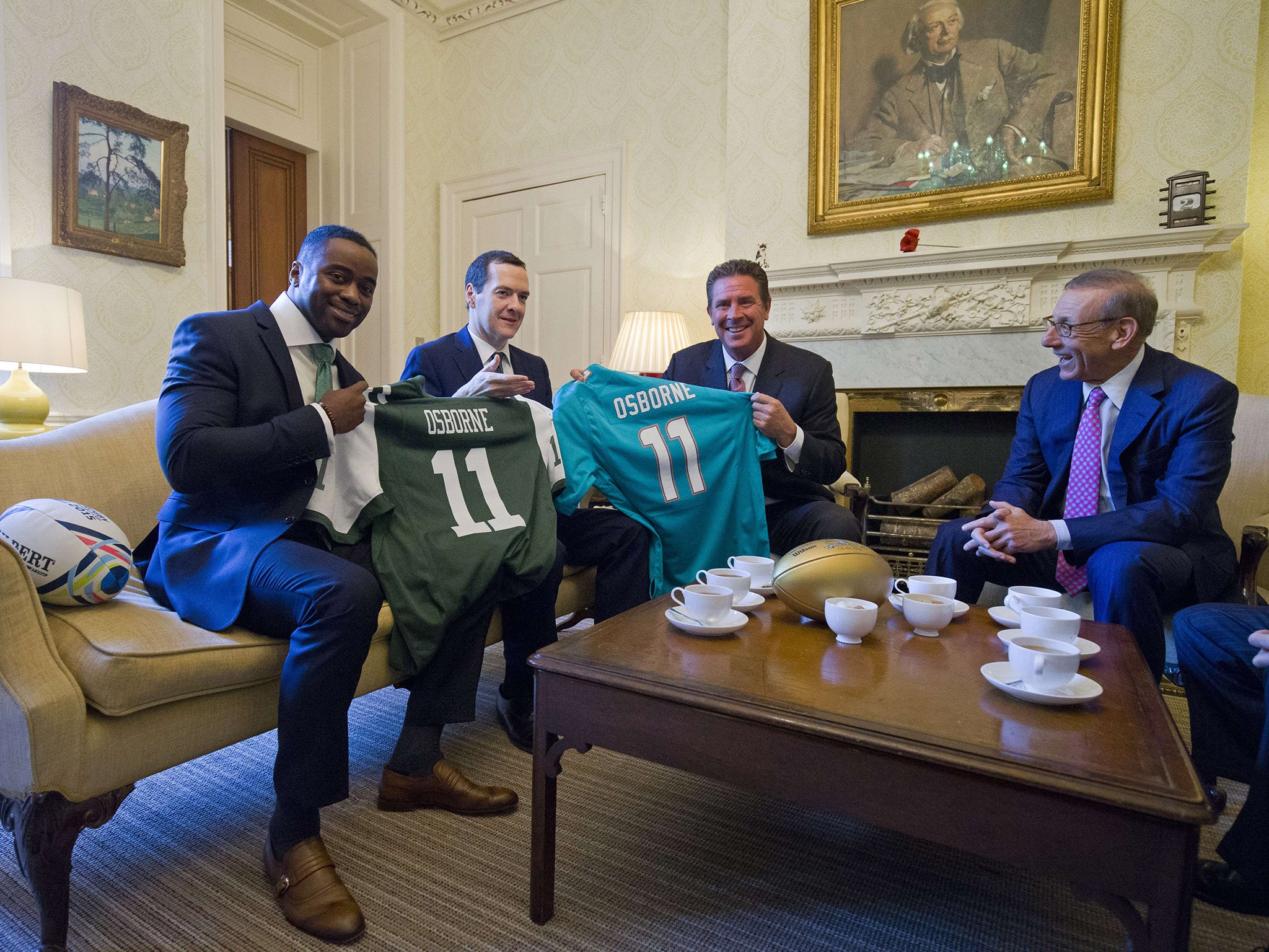 Former American footballers Curtis Martin (left) and Dan Marino put their shirts on George Osborne while quizzing him about the grade of paper they’ll find in the loo at 11 Downing Street