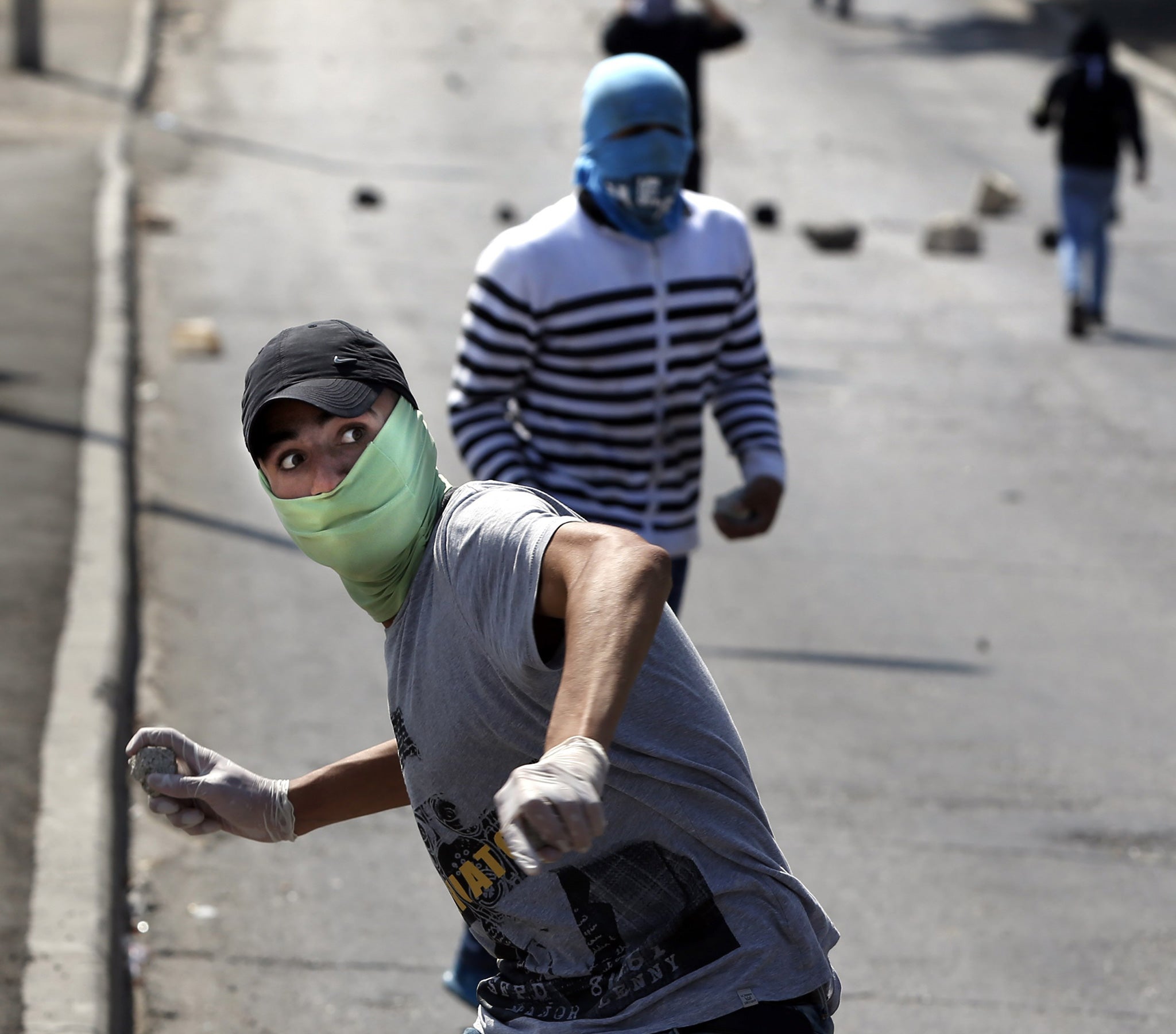 A Palestinian demonstrater throws stones towards Israeli security forces