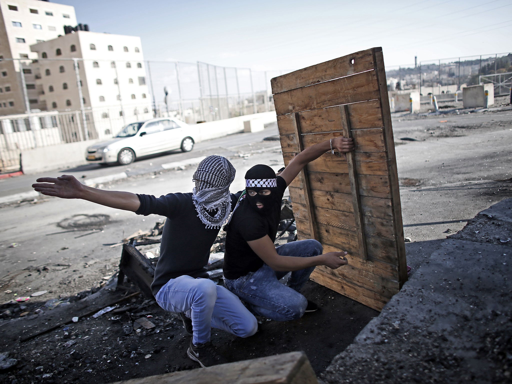 Palestinian demonstraters take shelter as they prepare to throw a molotov cocktail towards Israeli security forces