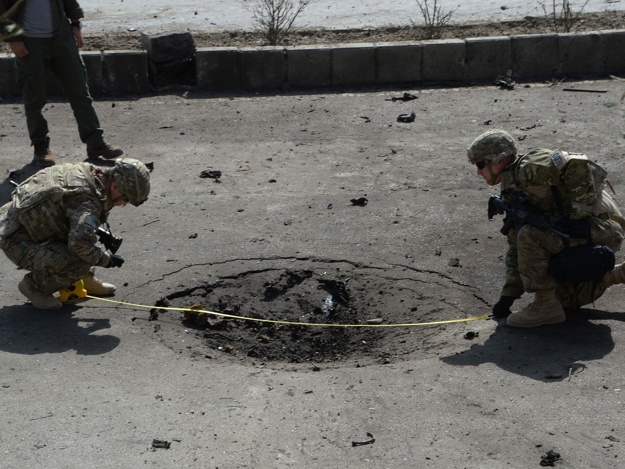 NATO soldiers measure a crater at the site of a bomb attack that targeted foreign military vehicles at Jo-e-Sher in Kabul on October 11, 2015.