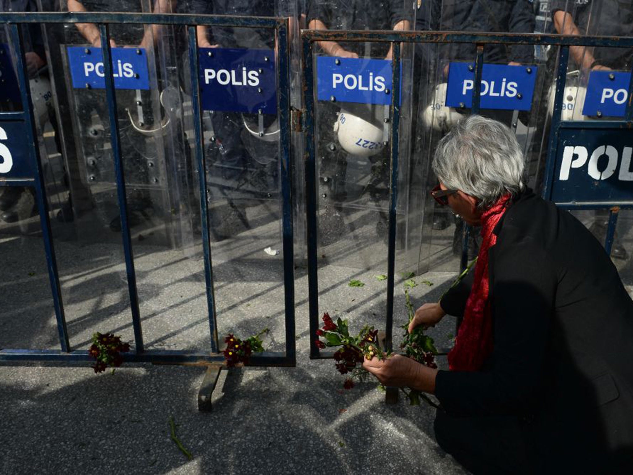 A protester leaves the carnations on the ground by a police barricade blocking the way to the site of Saturday's explosions