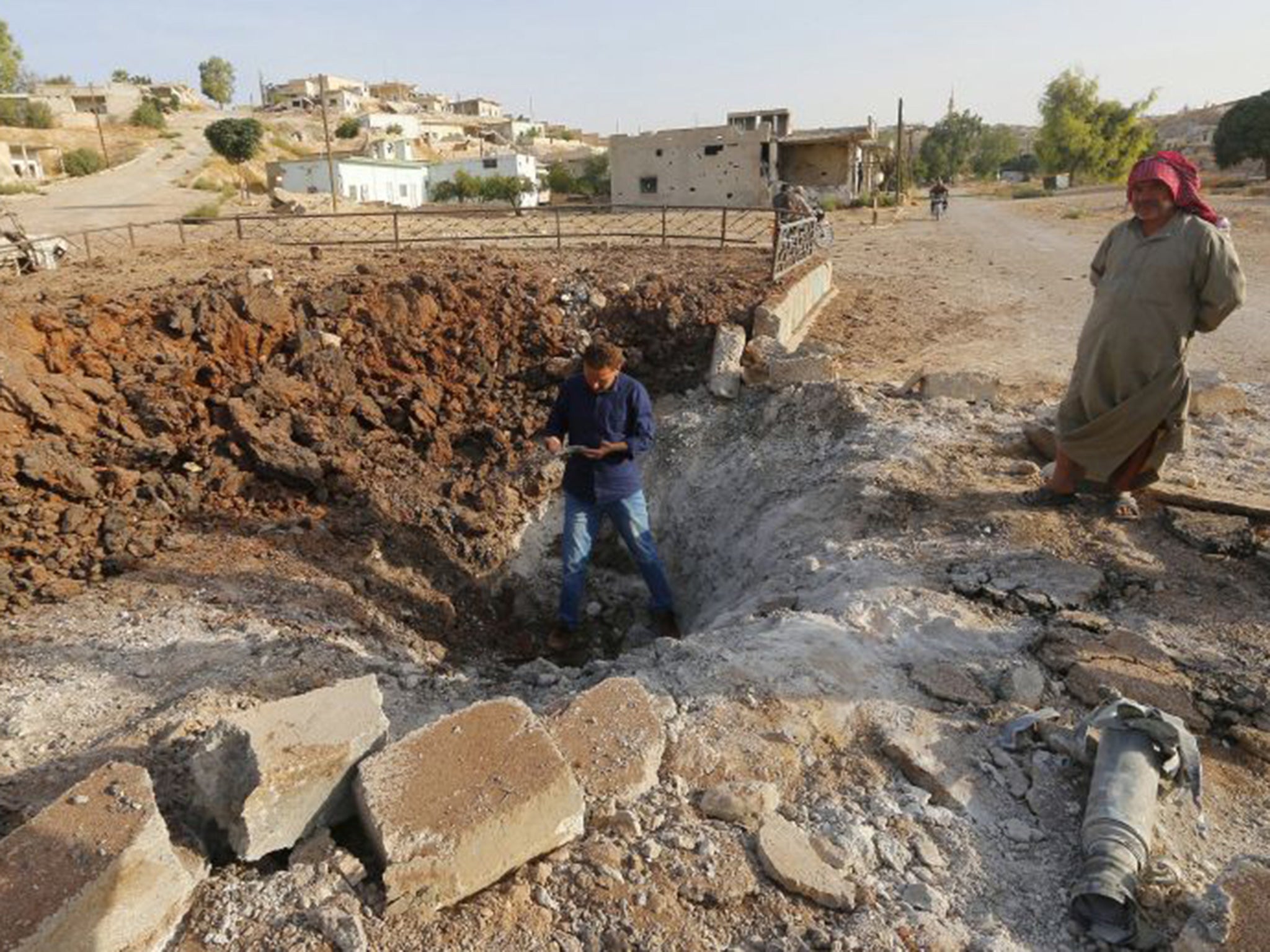 Men stand along a crater caused by what activists said was a Russian air strike in the northern countryside of Hama