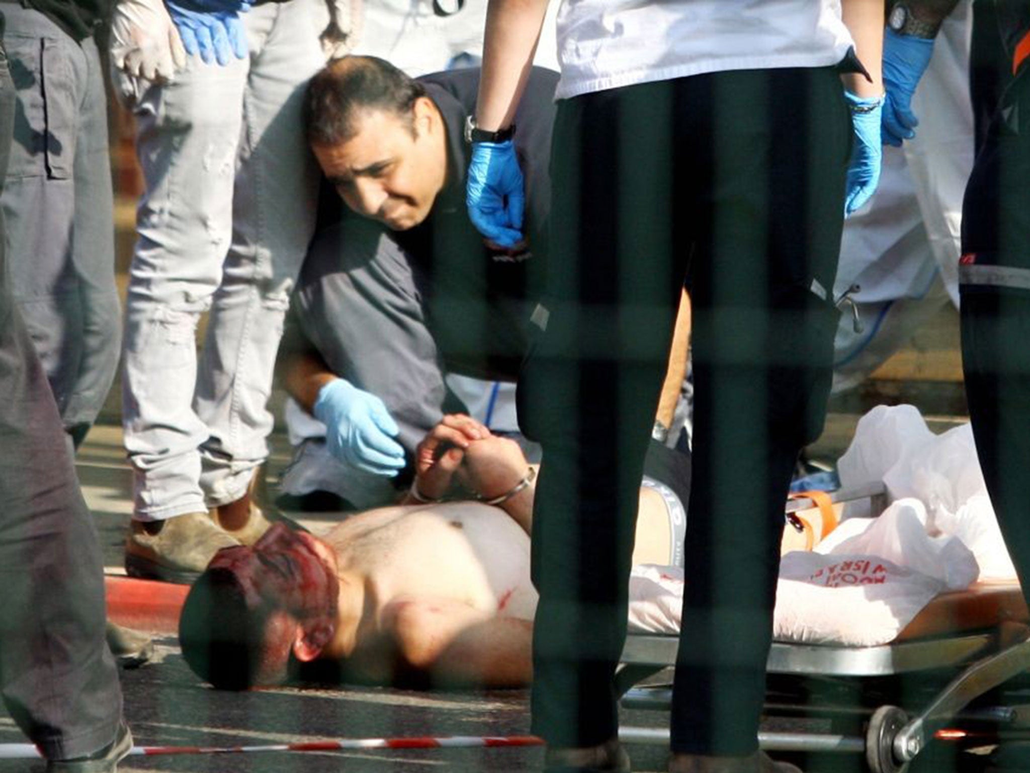 Israeli security forces stand next to a wounded and handcuffed Palestinian man who carried out the stabbing attack