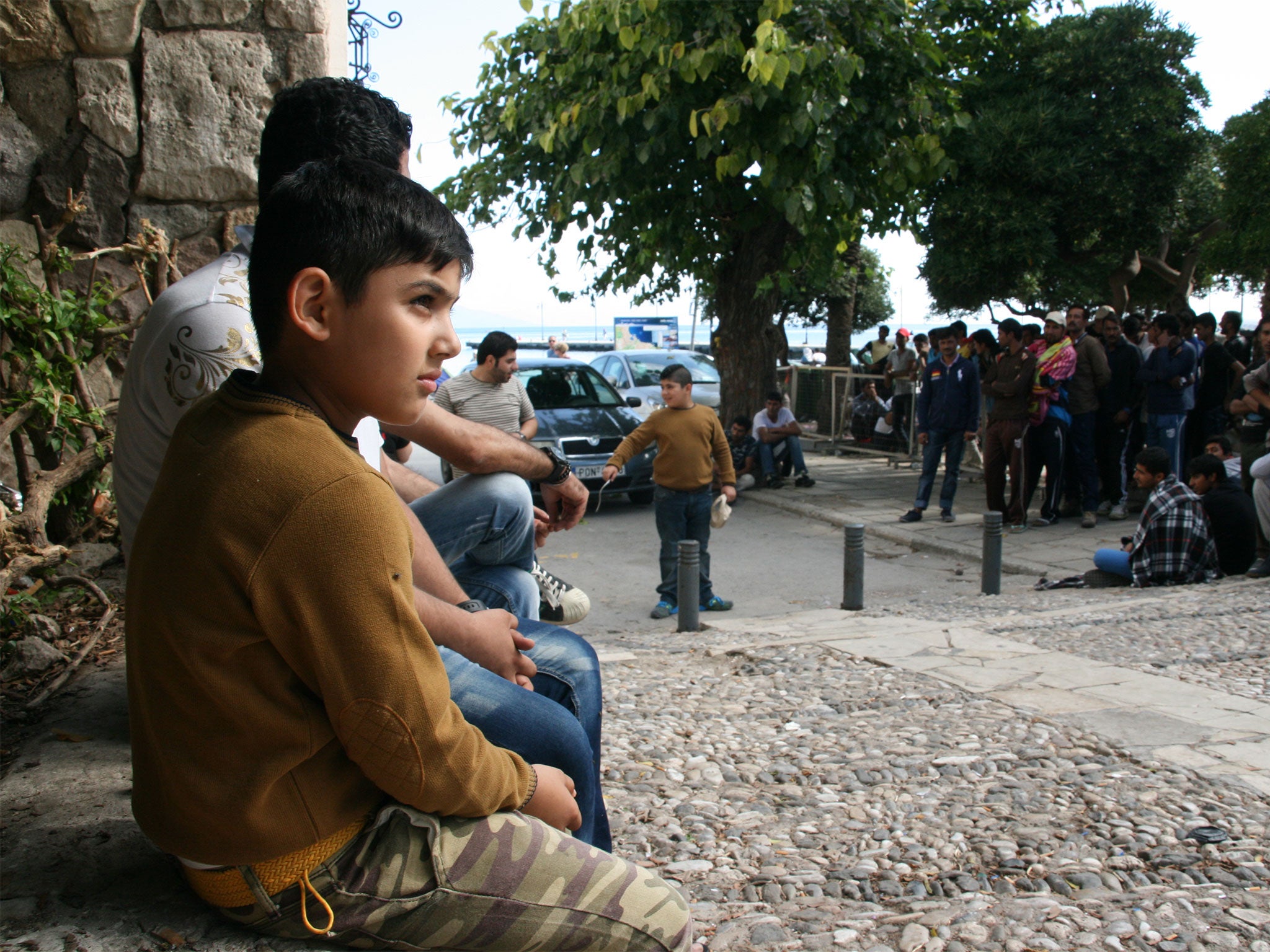 
A young Pakistani and his family wait on the curb outside the downtown Kos police station where refugees must register upon arrival on the island (Photo by Cody Punter)