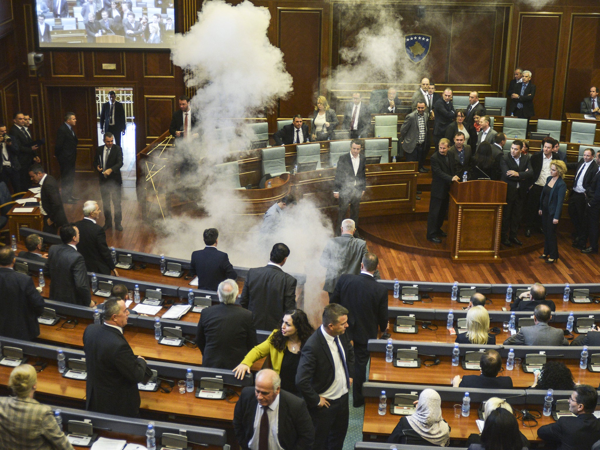 Parliamentarians disperse as a white cloud of tear gas rises after being released by opposition lawmakers in Kosovo's parliament in Pristina.