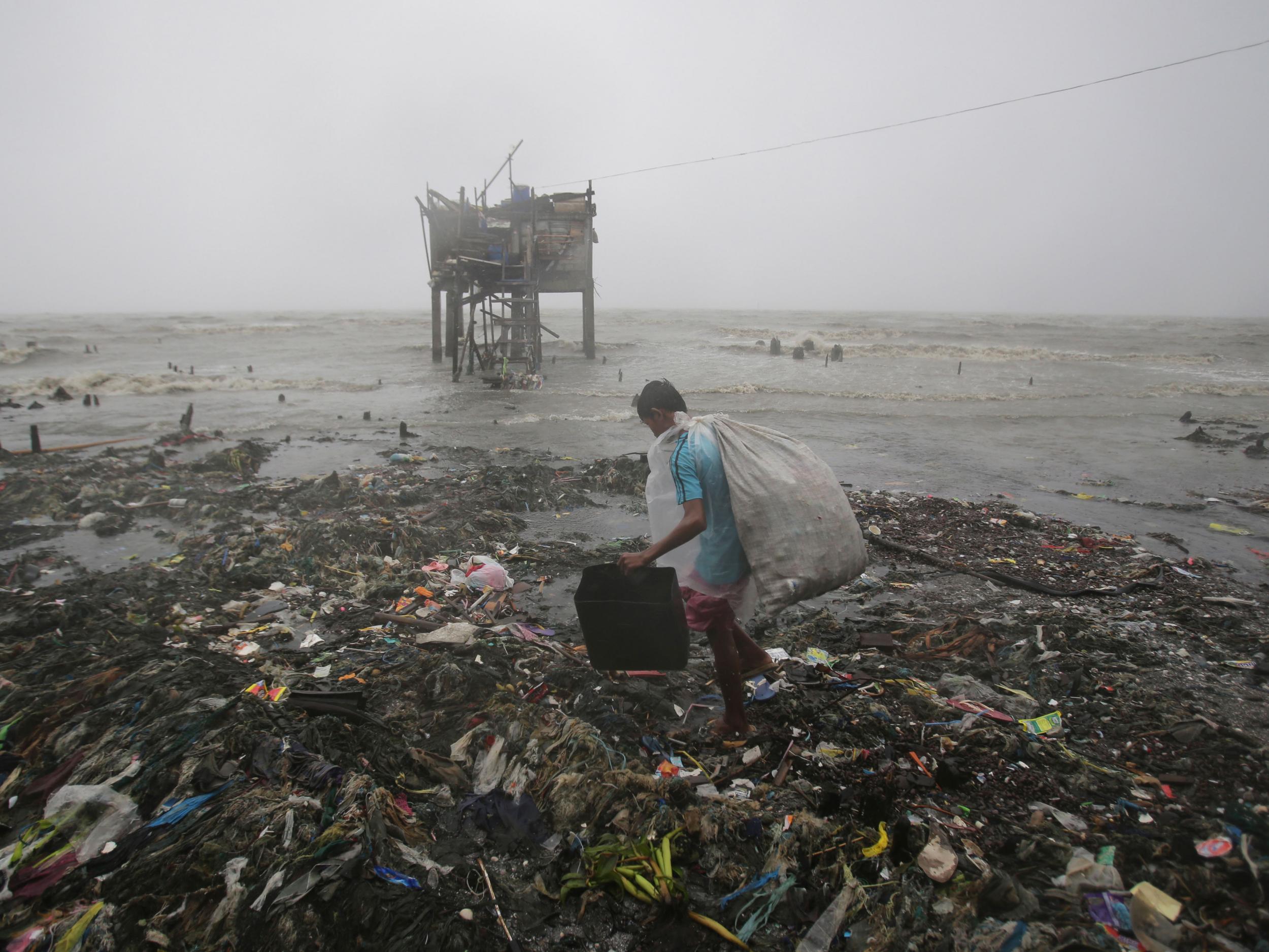 A Filipino man scavenges recyclable materials near a house on stilts stands by the bay amid strong winds and rains caused by Typhoon Koppu