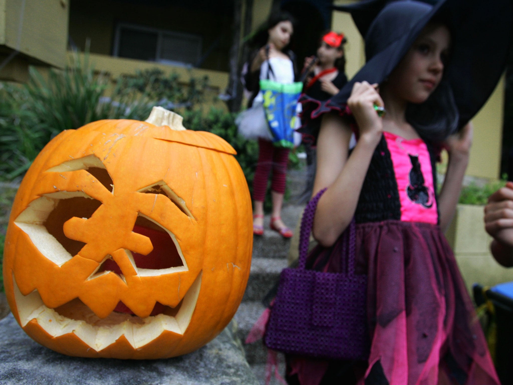 A pumpkin is seem out front of a home as children trick or treat though streets on Halloween Day