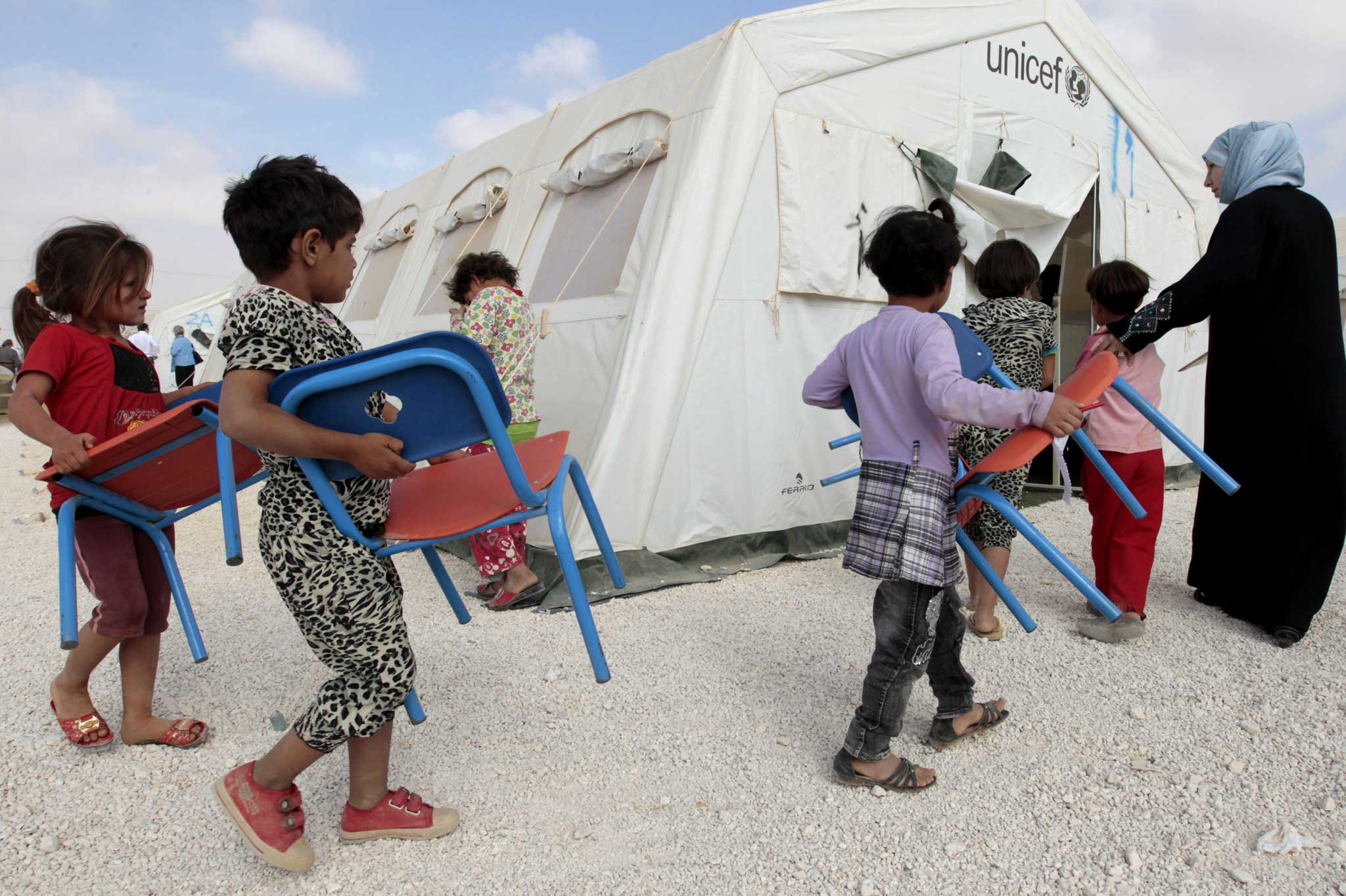 Syrian children bring their chairs to class in a refugee camp