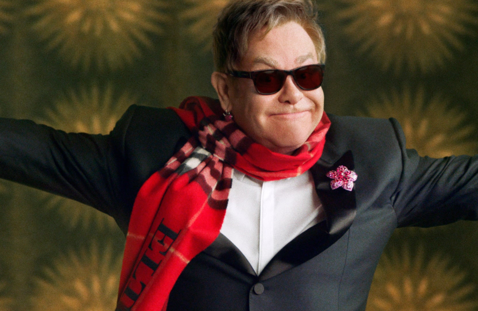 Elton John in the Burberry Festive Film wearing a red scarf with name emblazoned on it