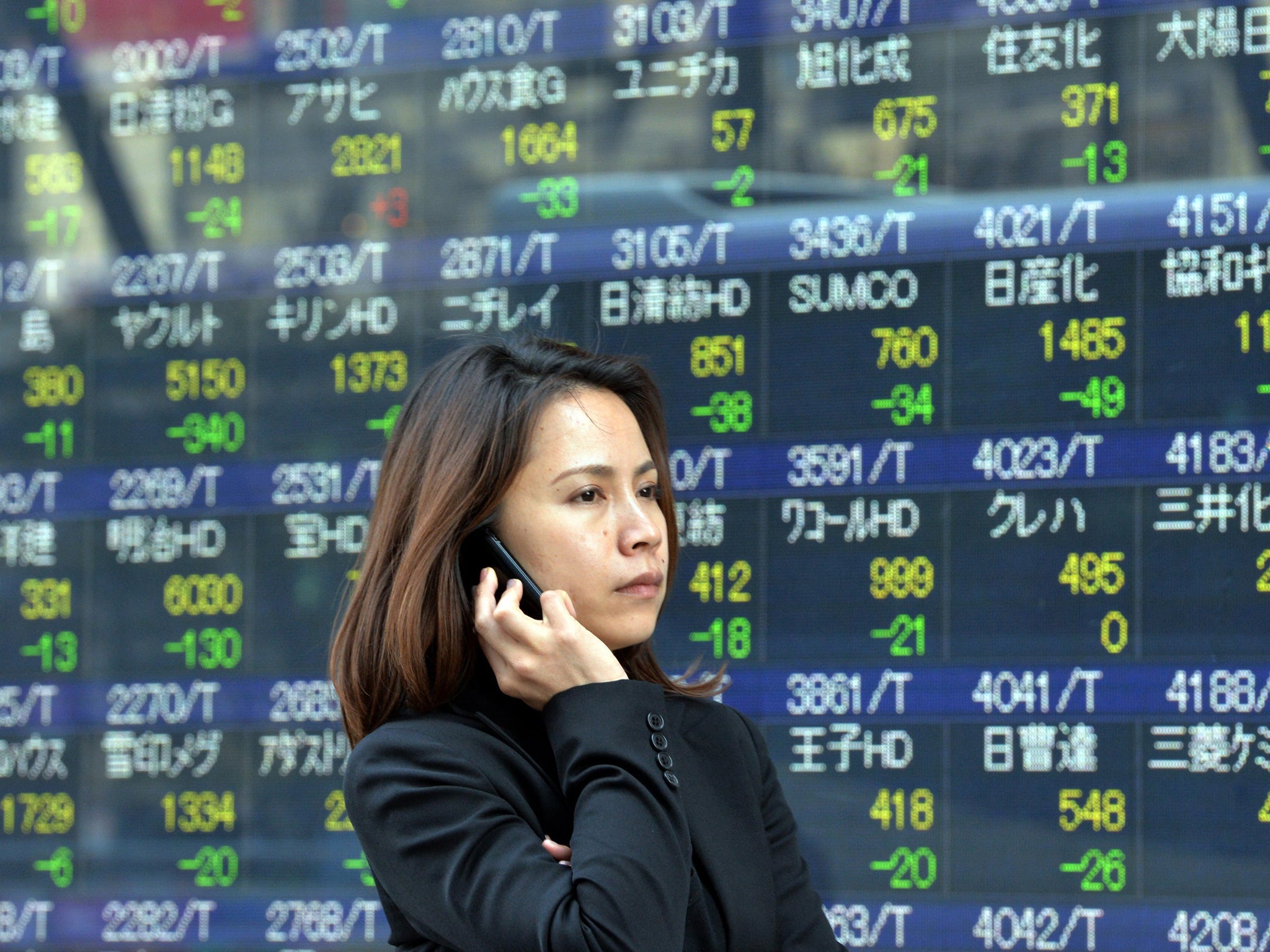 A woman uses her mobile phone before a share prices board in Tokyo on May 7, 2014.