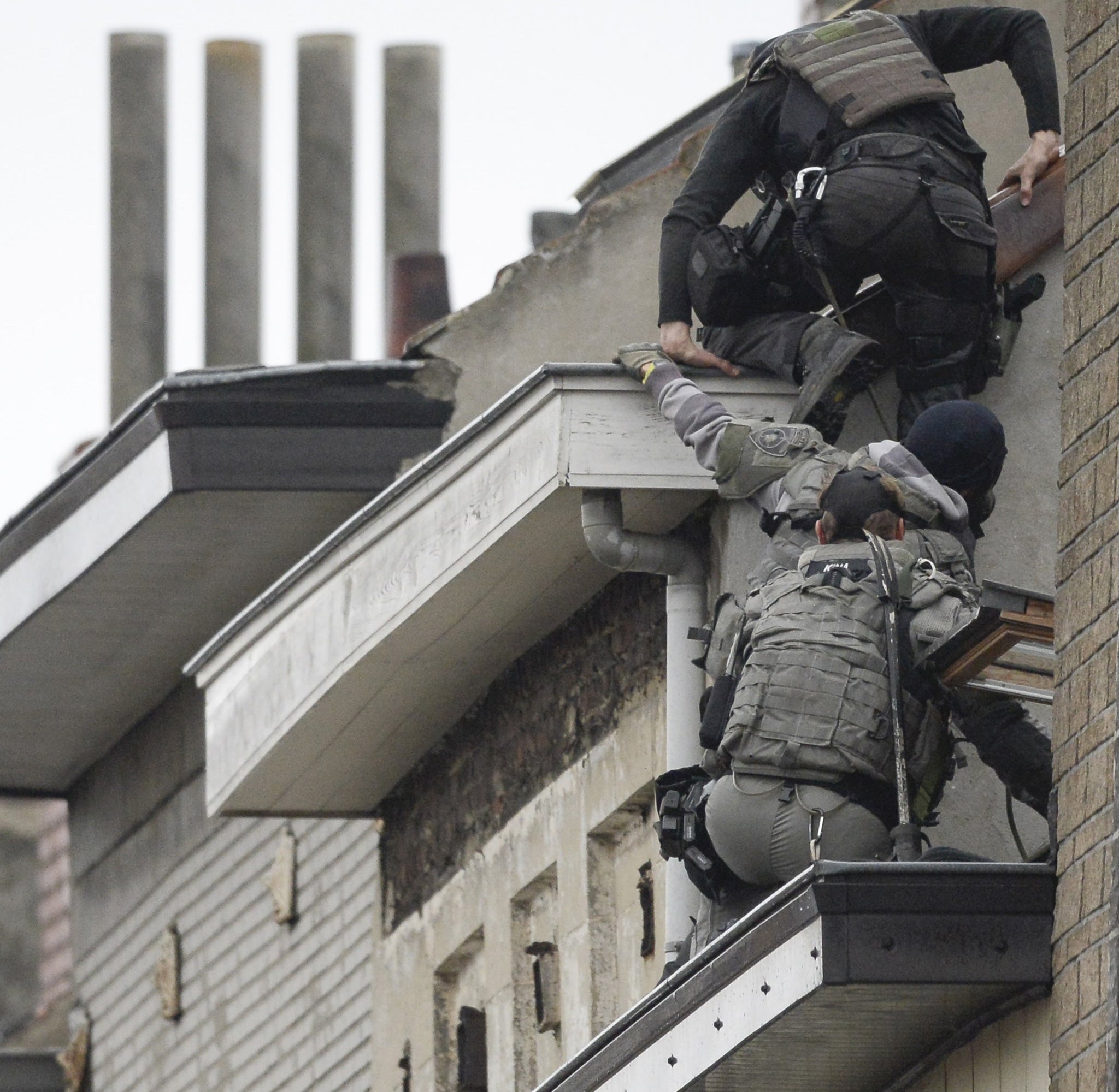 Security forces personnel move in from balconies to a building being entered as part of ongoing operations in the Molenbeek district of Brussels on 16 November, 2015