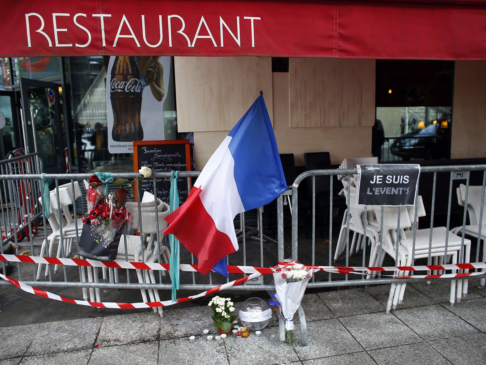 The French flag and floral tributes are displayed on a barrier near a restaurant hit by the terror attacks near the Stade De France stadium in Saint-Denis