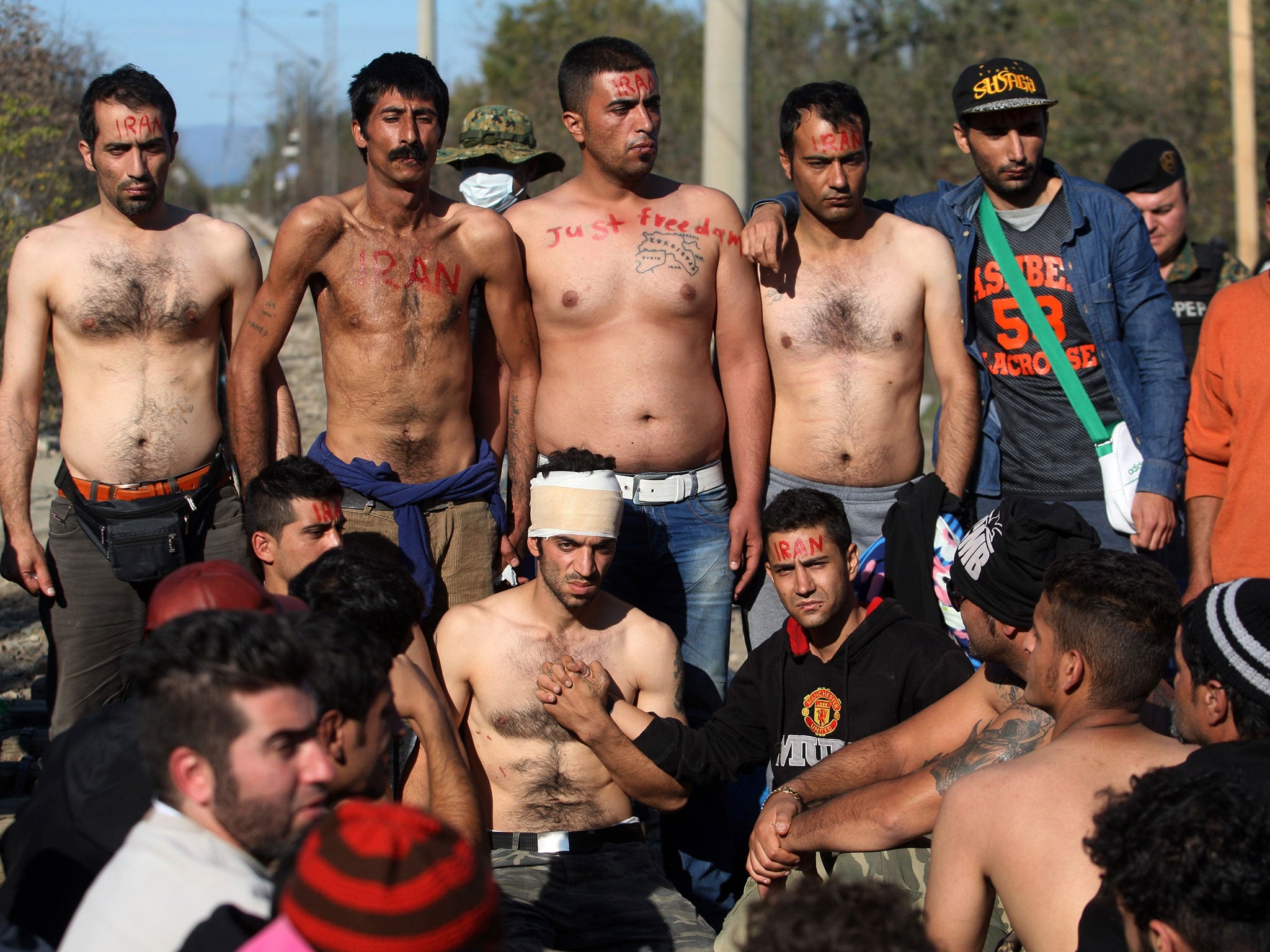 Migrants and refugees from Iran with their mouths sewn shut sit on railway tracks as they wait to cross the Greek-Macedonian border on 23 November