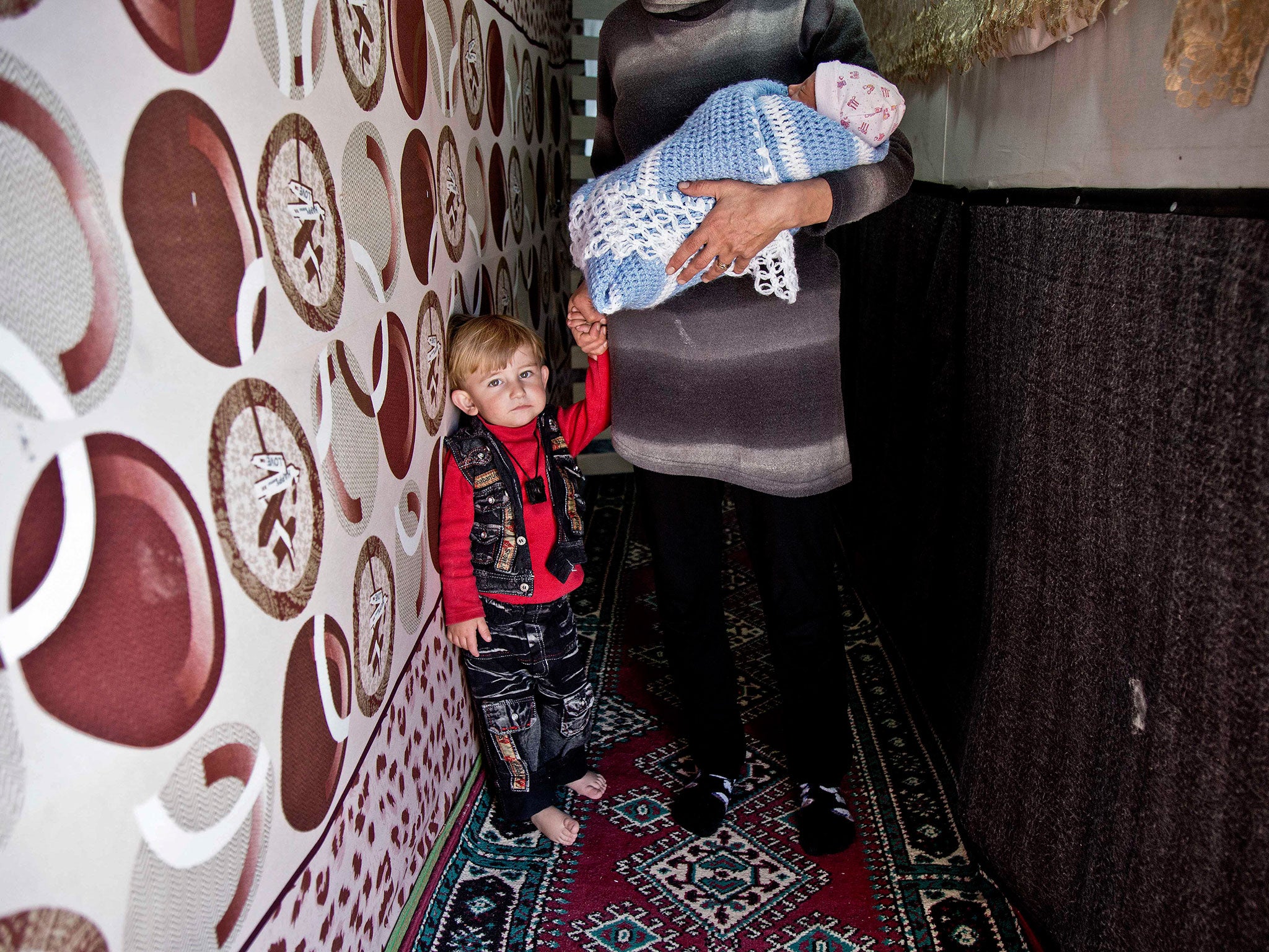 A 28-year-old Syrian refugee woman holds her children, at an informal tented settlement