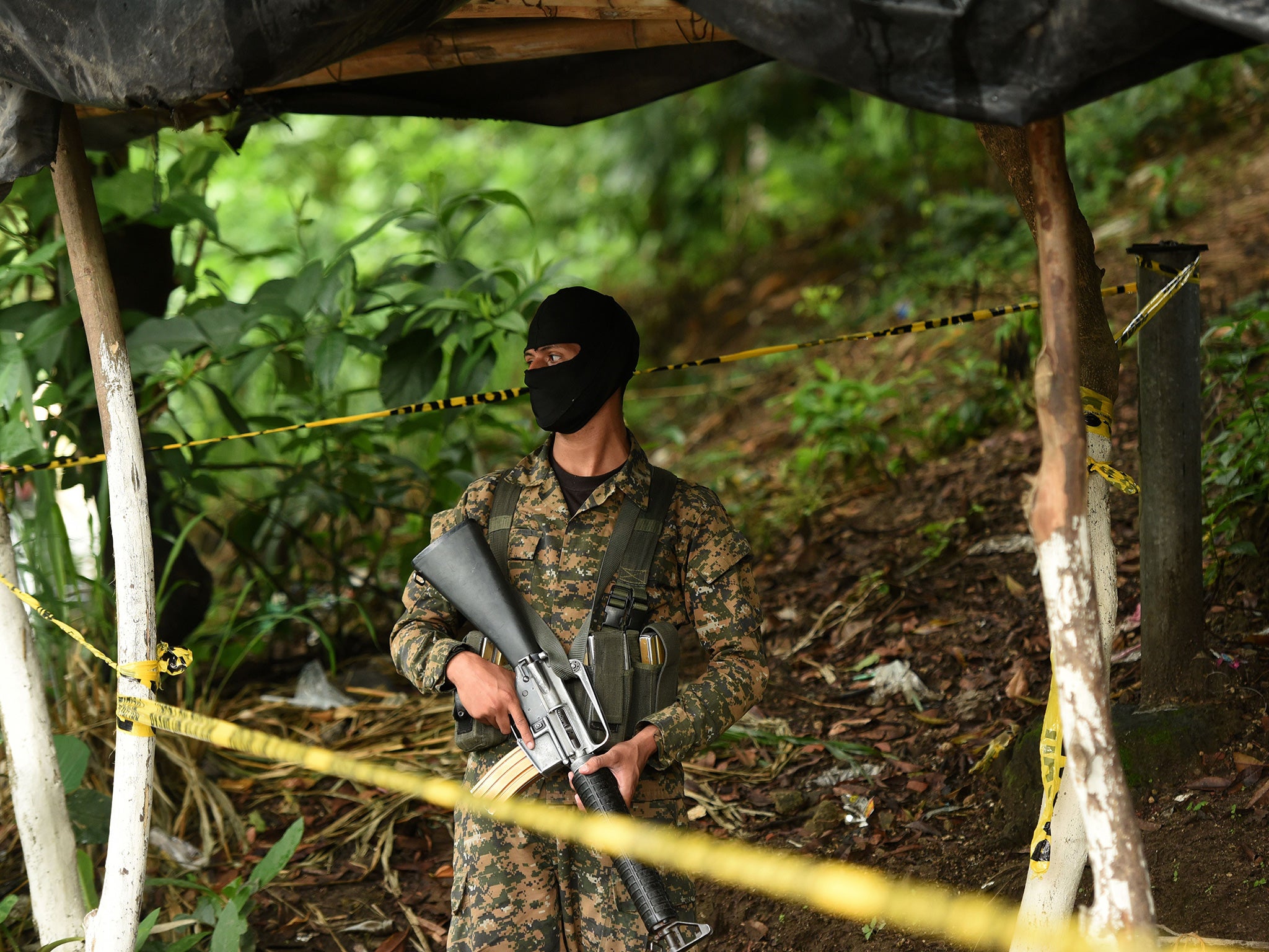 A soldier stands guard at a crime scene where three bus drivers and another man were killed by alleged members of the Mara 18 street gang, one of the gangs involved in the prison fight