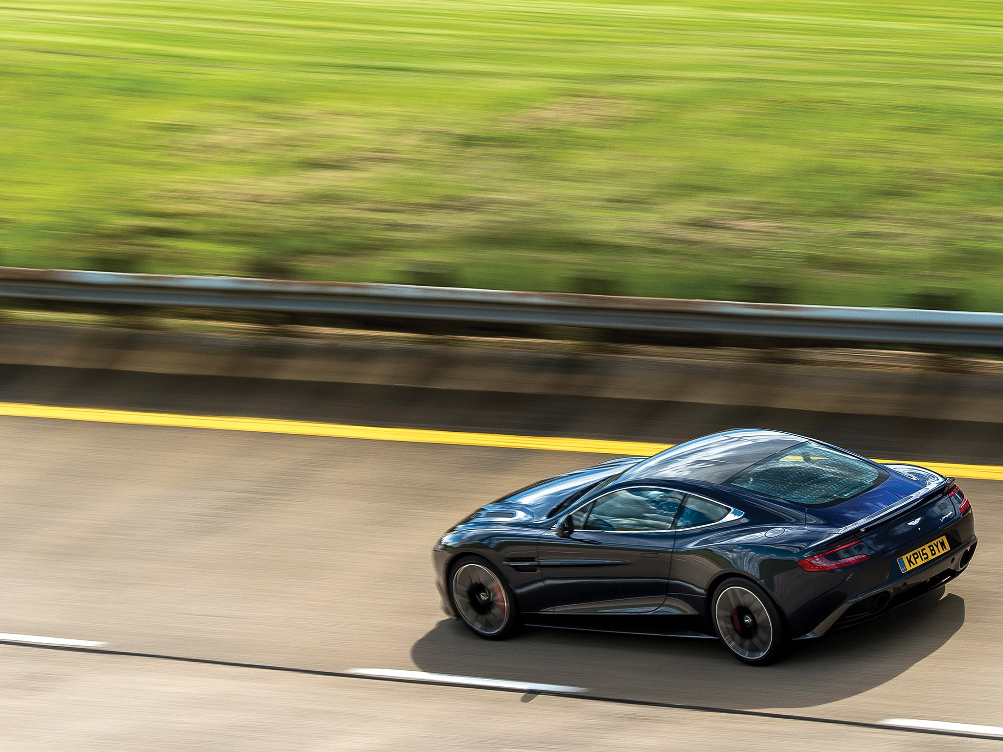 An Aston Martin darts across a country road