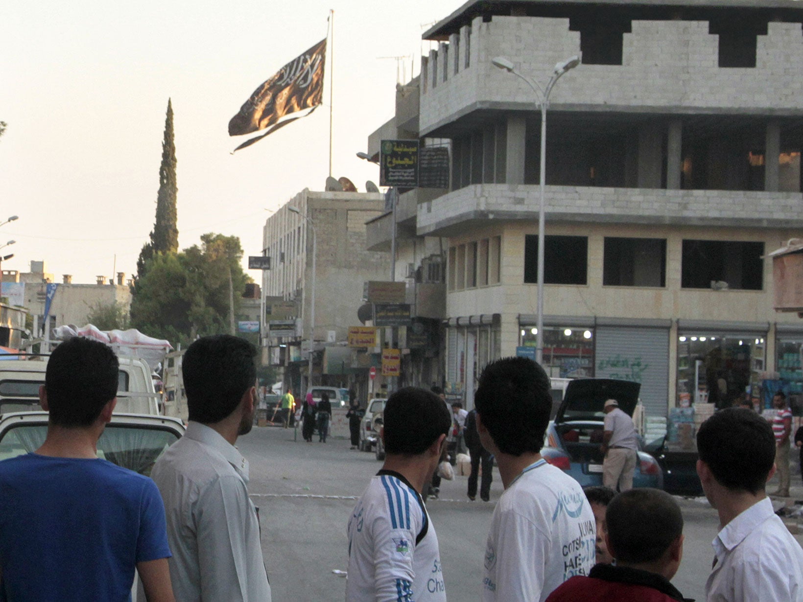 Men look at a Jihadist flag over a building in the rebel-held Syrian city of Raqqa Getty