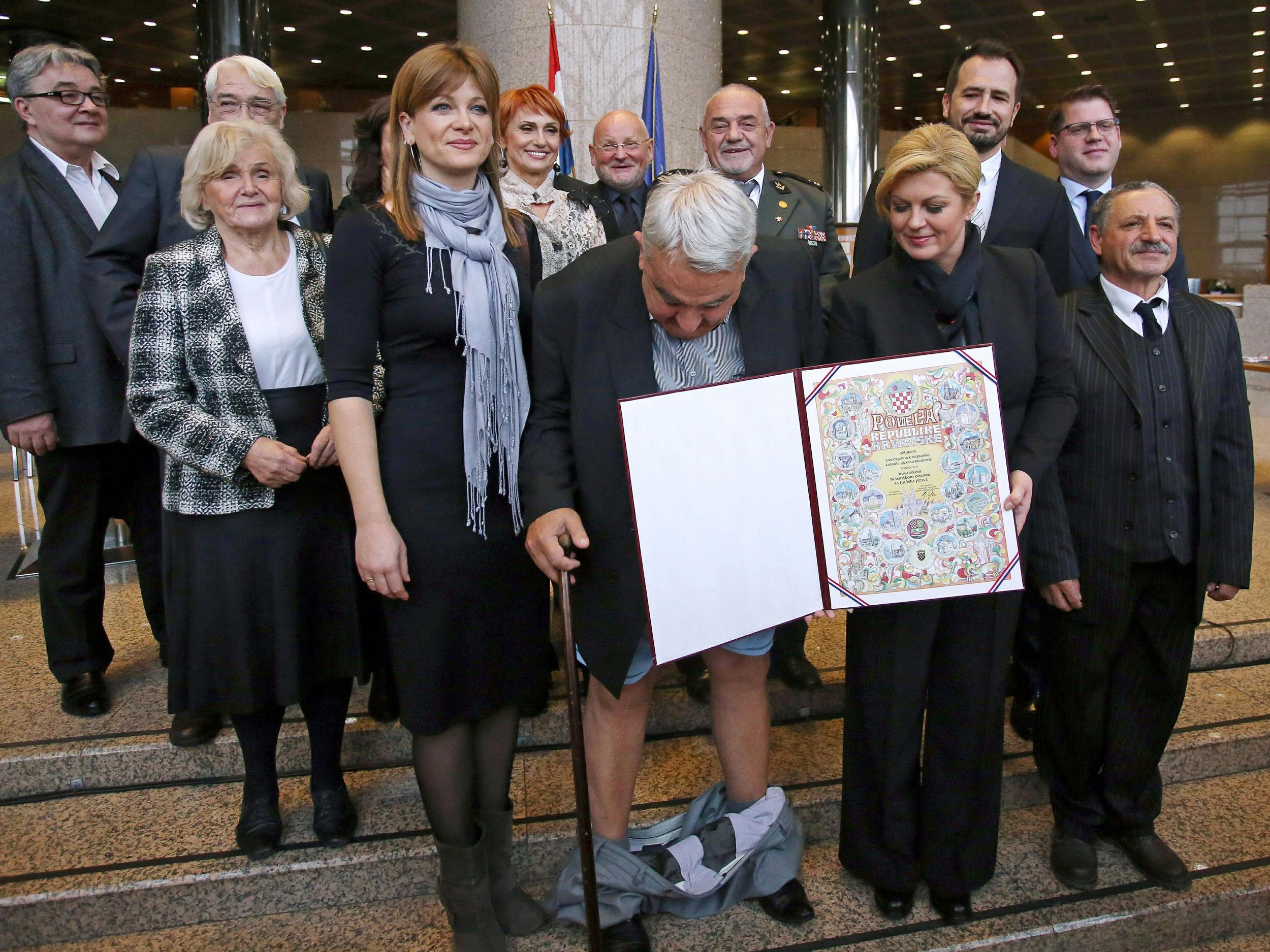 Croatia's leading rights group chief Ivan Zvonimir Cicak's looks down after his trousers fell down while posing for a photo with Croatian President Kolinda Grabar-Kitarovic