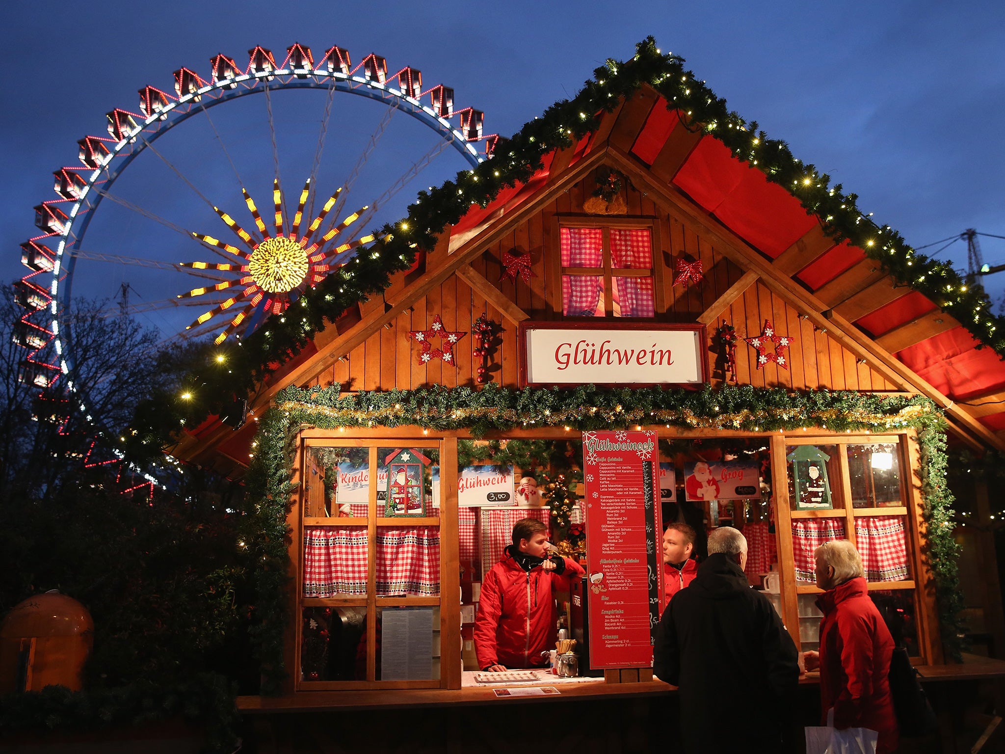 Visitors stop at a stall selling glühwein next to an illuminated ferris wheel at the Christmas market at Alexanderplatz