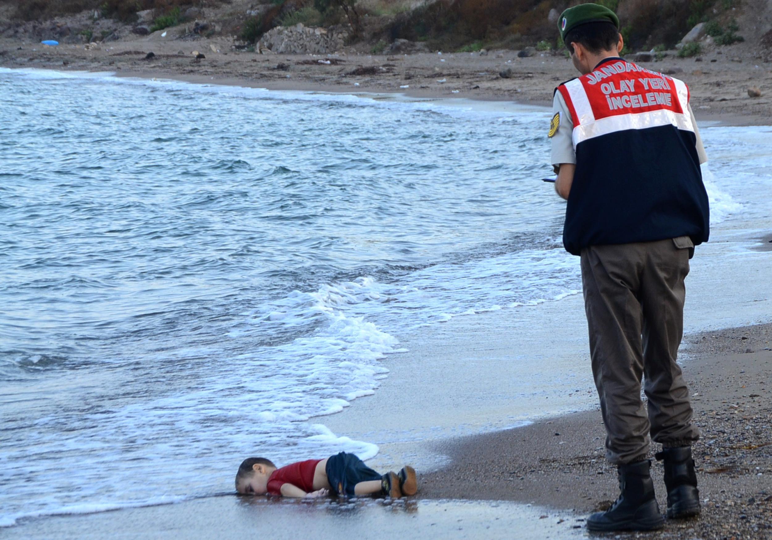 A Turkish police officer stands next to Alan Kurdi's body