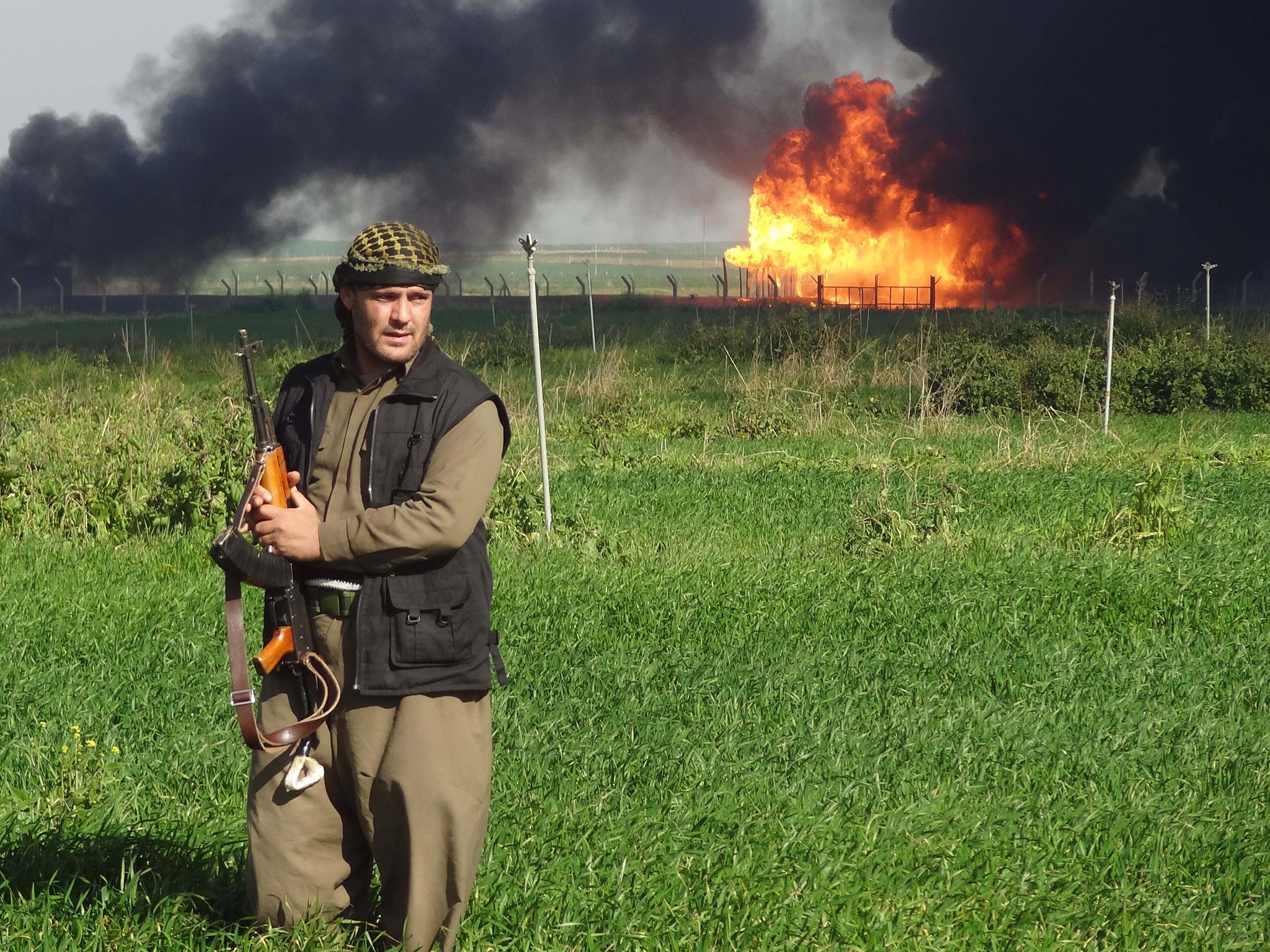 A member of the Kurdish Peshmerga forces walks at the Khubbaz oil field as smoke billows in the background on a fews days after Peshmerga forces and police retook the area from Isis