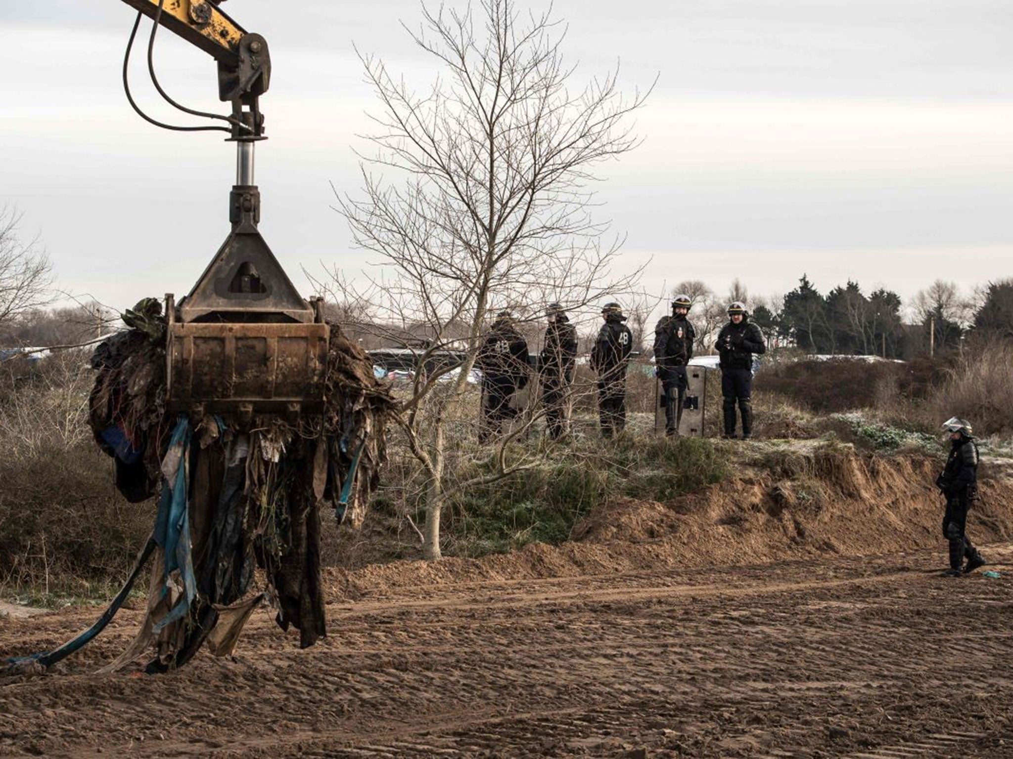 A bulldozer clears a part of a makeshift camp known as "the jungle" under the surveillance of anti-riot police forces, on January 18, 2016 in Calais.