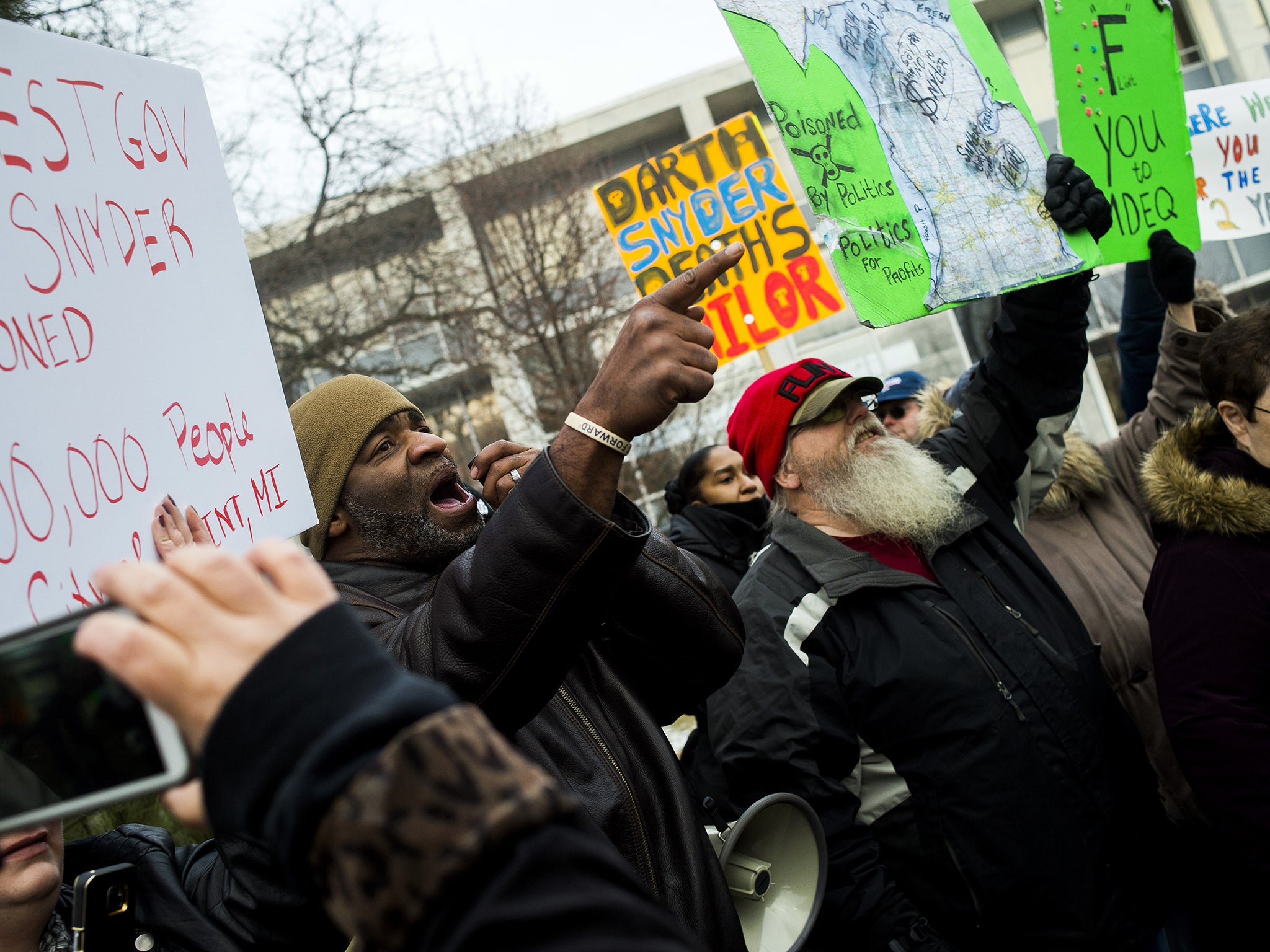 Flint residents Arthur Woodson, left, and Tony Palladino Jr. protest the arrival of Flint native and filmmaker Michael Moore as Moore accuses Gov.Rick Snyder of poisoning Flint water during a rally outside of city hall in Flint