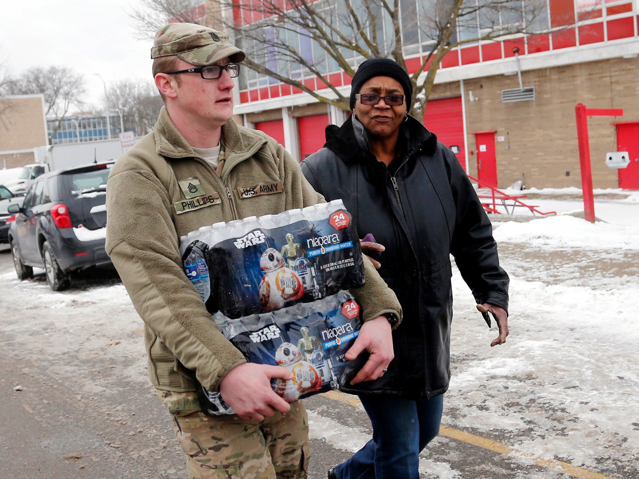 Michigan National Guard Staff Sergeant William Phillips (L) assists a Flint resident with bottled water at a fire station in Flint