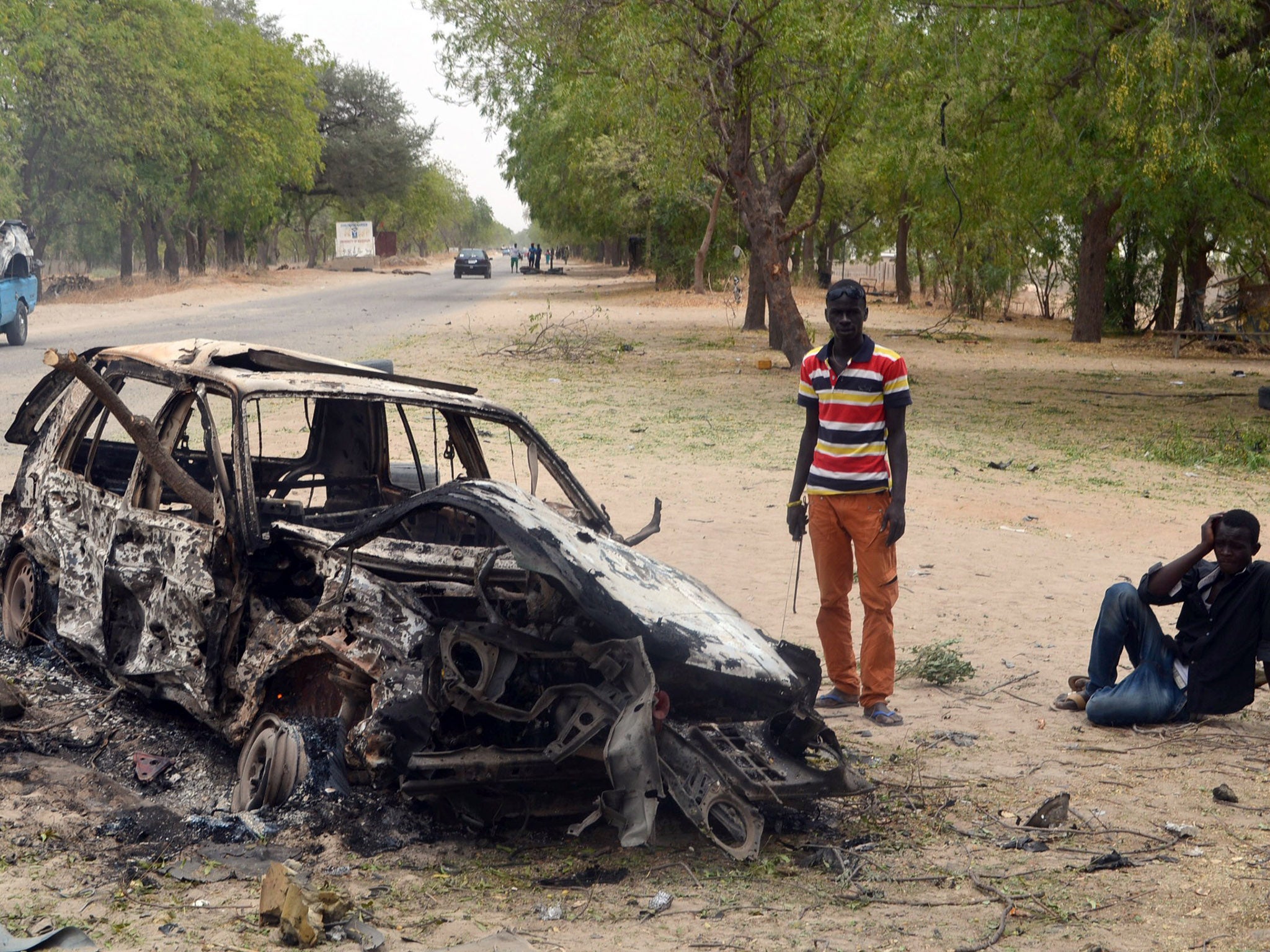 Two men next to a burnt out car in Maiduguri after a bomb attack by Boko Haram