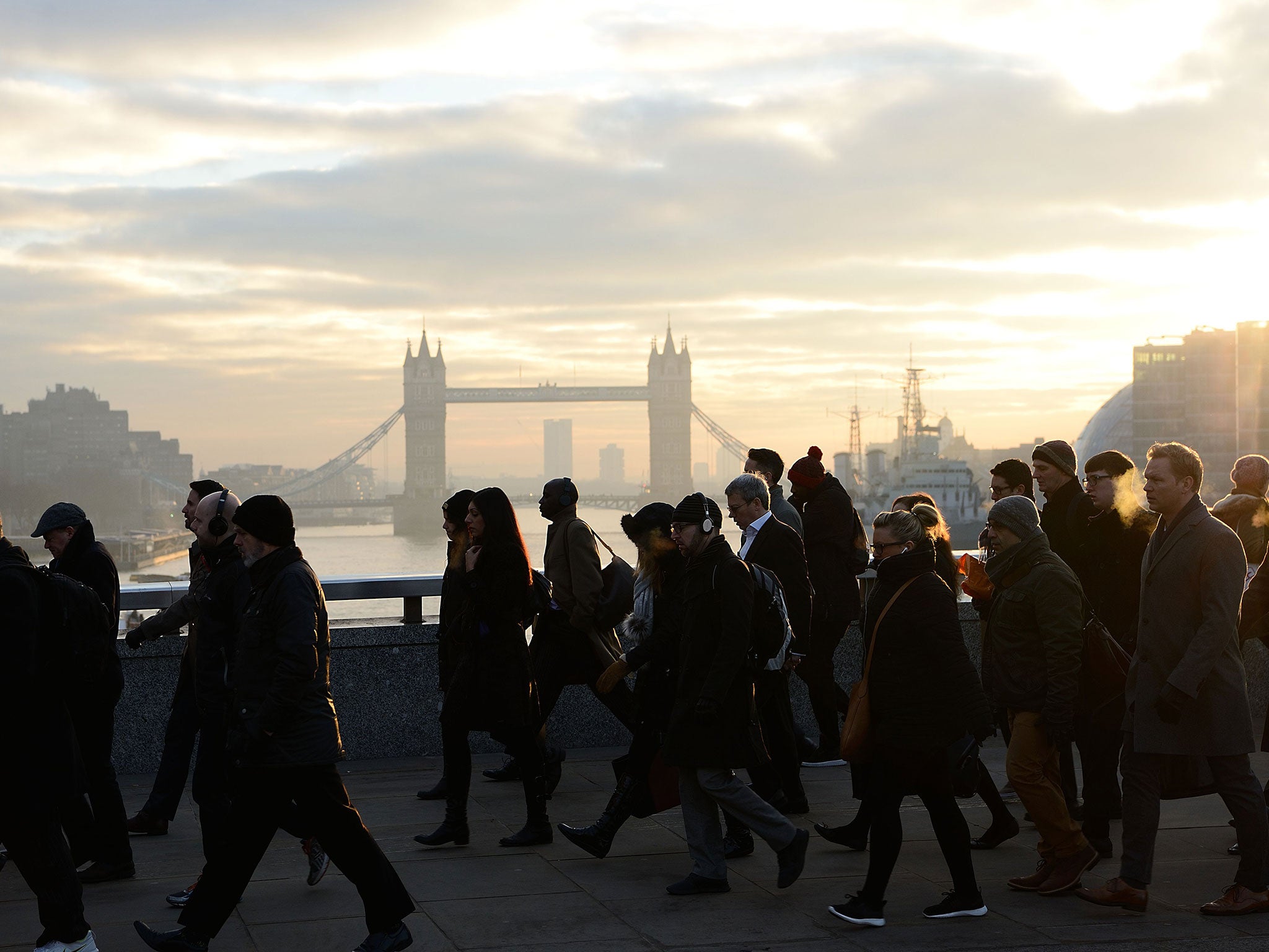 Commuters walk on London Bridge at sunrise with Tower Bridge in the background