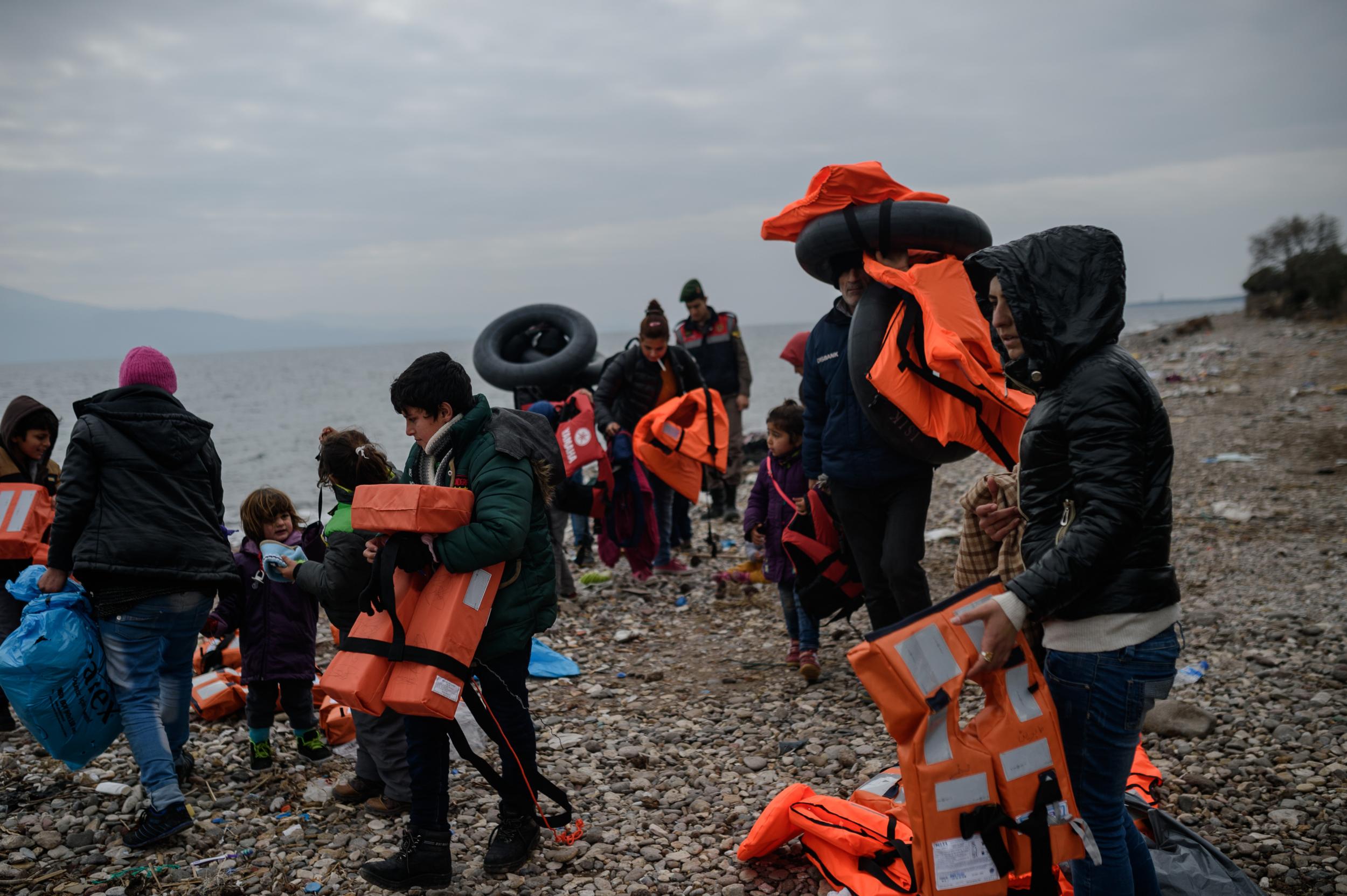 Syrian migrants holding life vests gather onto a pebble beach in the Yesil liman district of Canakkale, northwestern Turkey, after being stopped by Turkish police in their attempt to reach the Greek island of Lesbos on 29 January 2016.