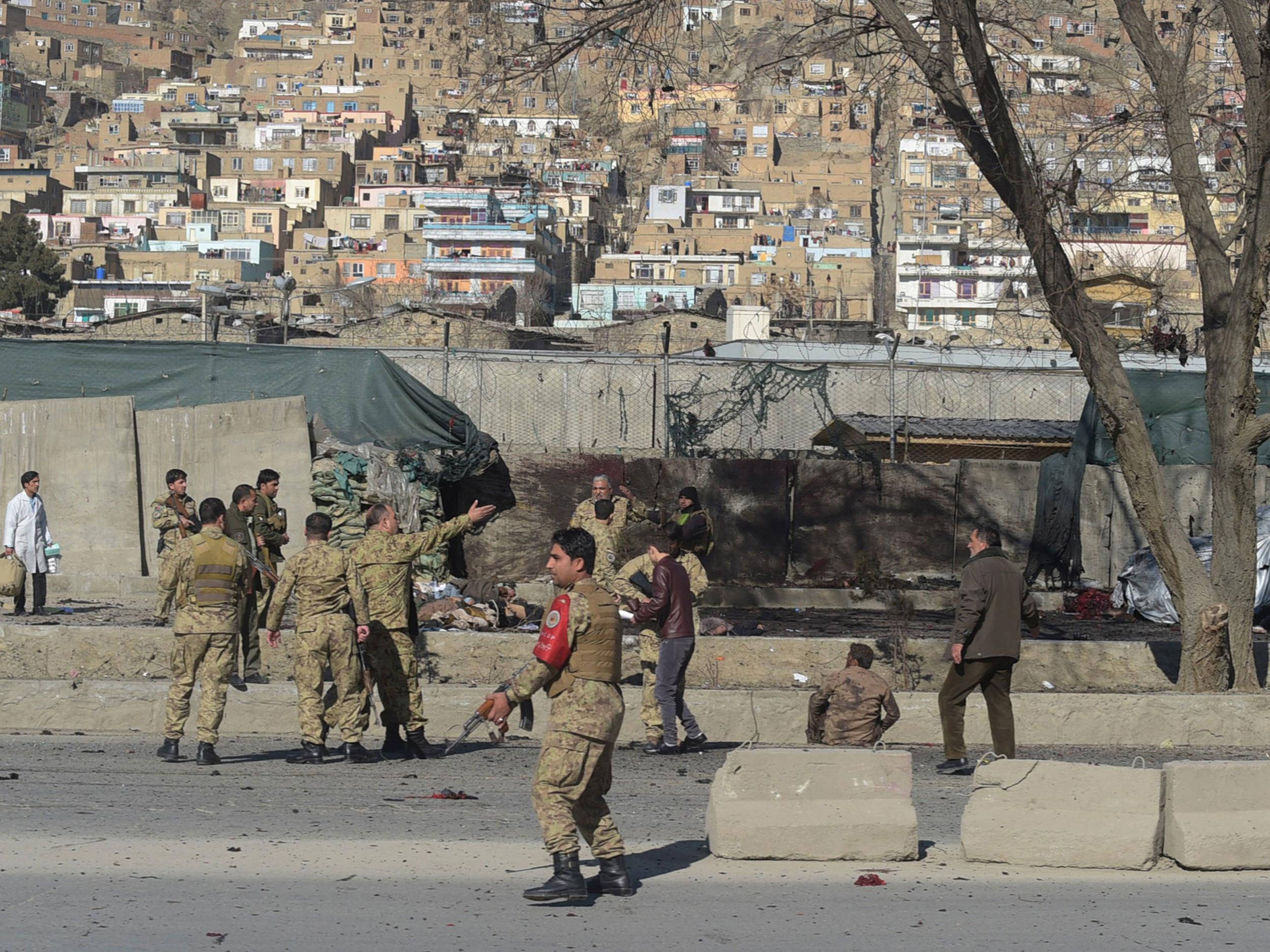 Afghan security personnels gather as victims are treated at the site of a suicide car bomb next to a police base in Kabul