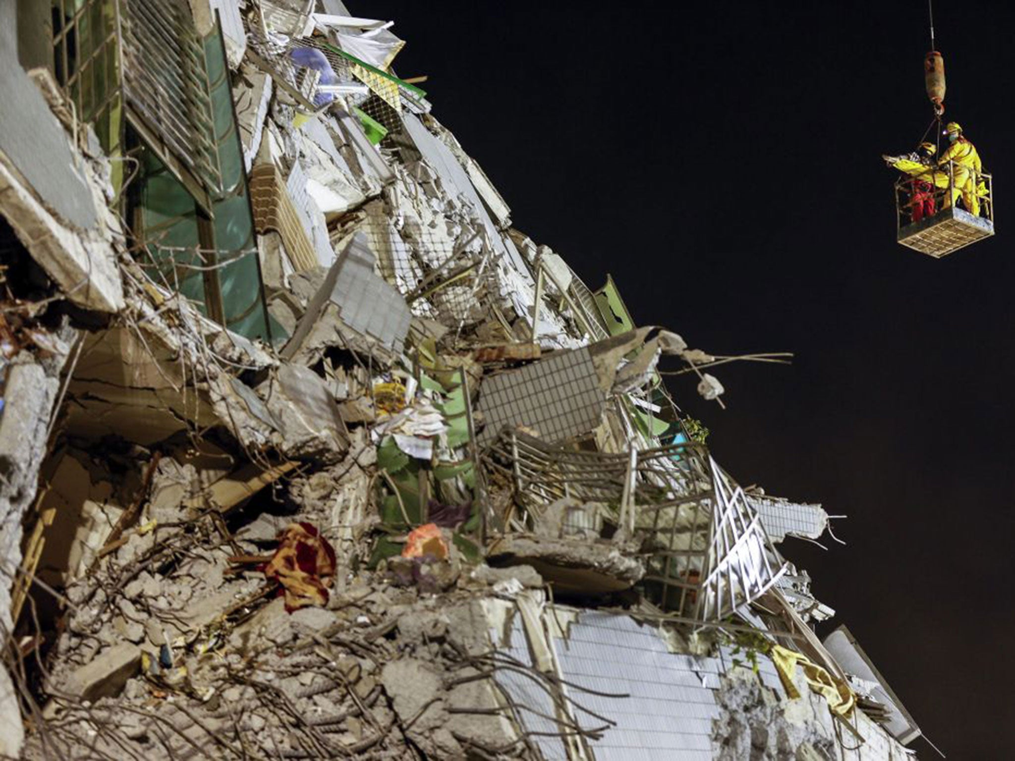 A crane lifts rescuers up to a collapsed building