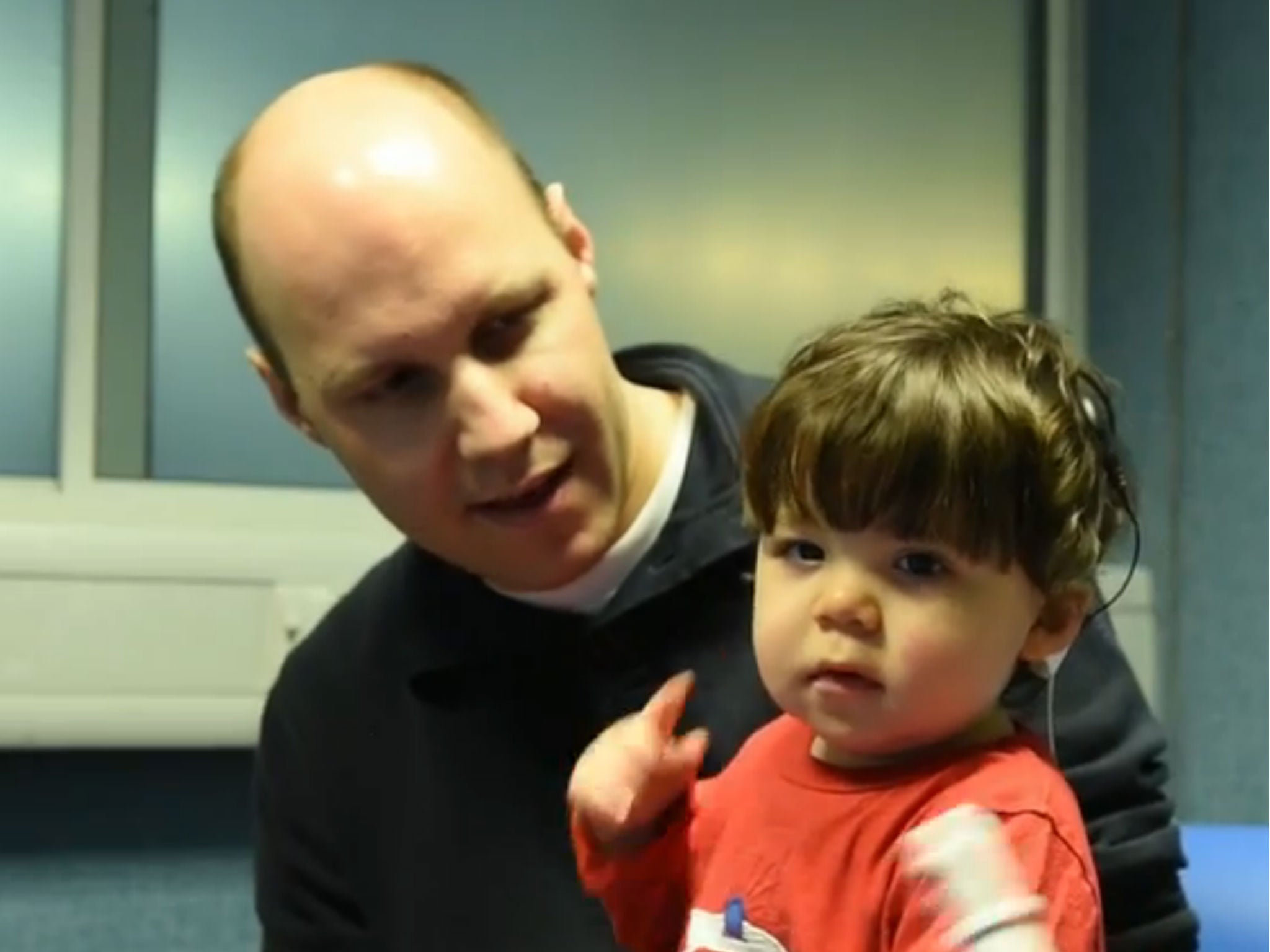 Alfie sits on his fathers knee while his new cochlear implant fitted and switched on for the first time