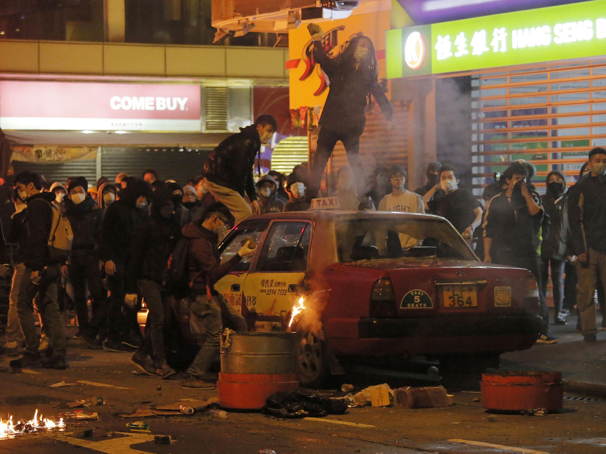 Demonstrators mount a burning taxi