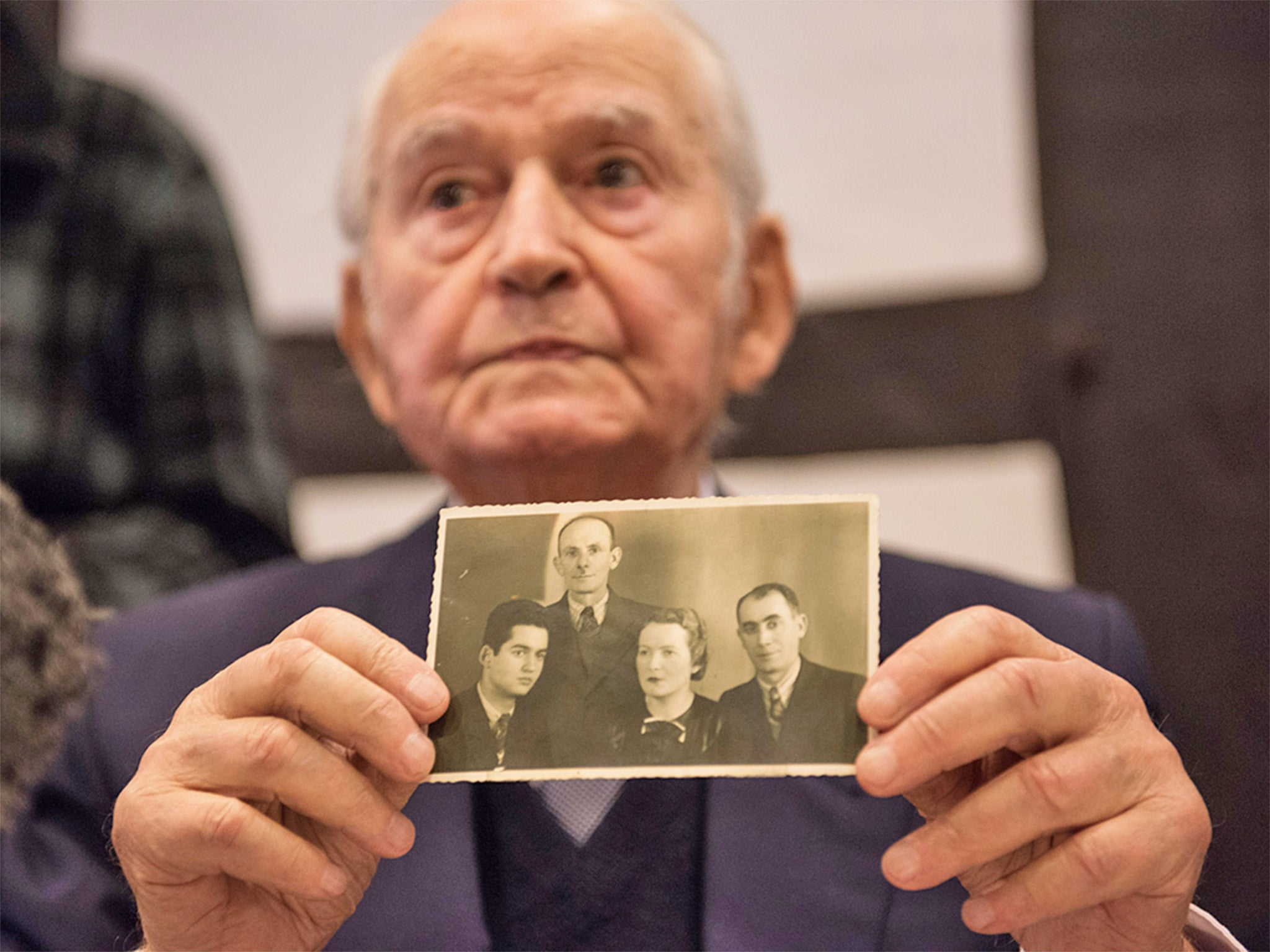 Leon Schwarzbaum at a press conference with a photograph of himself (left) with his uncle and parents, who died in Auschwitz