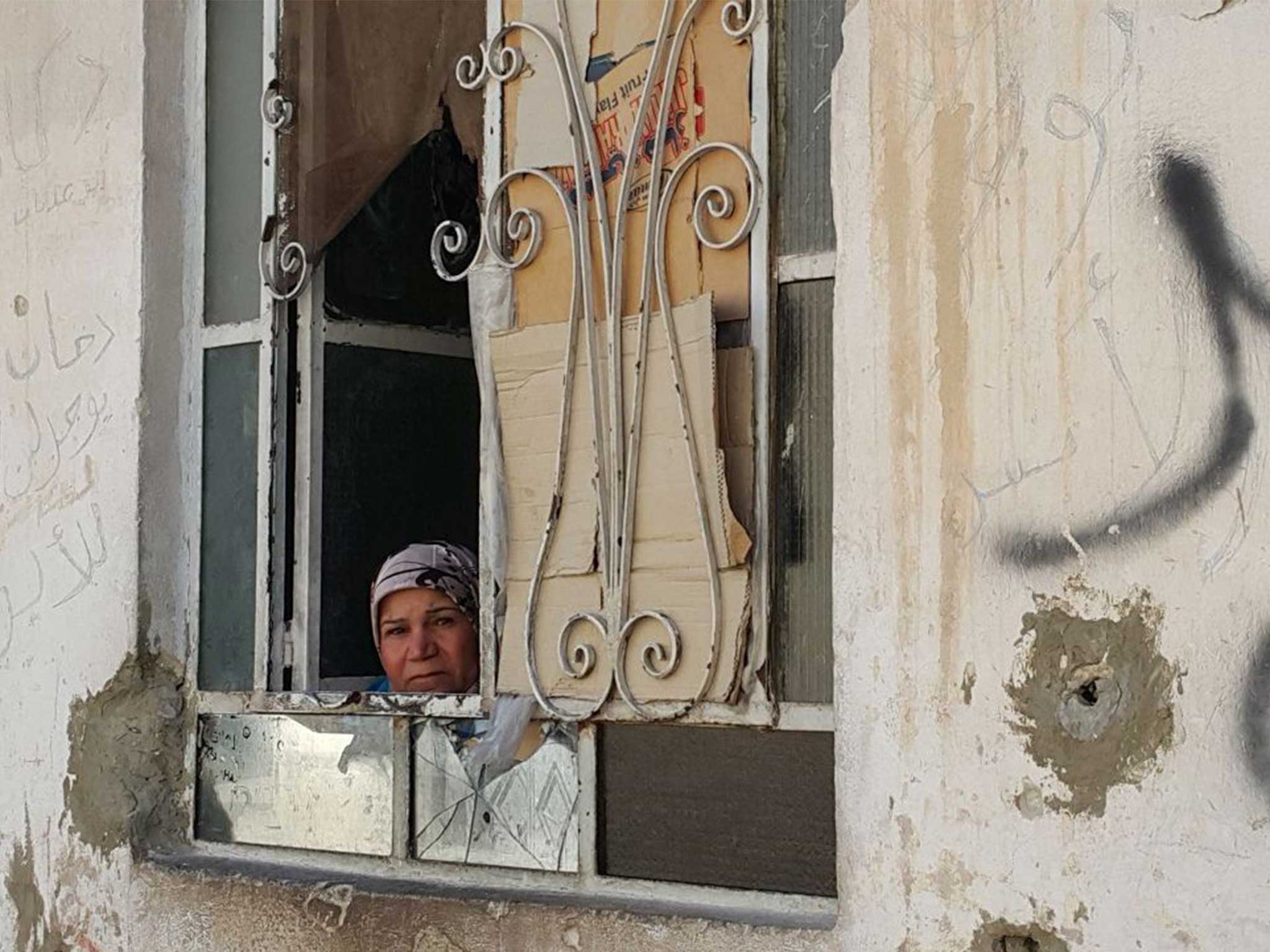 A woman peers out of her window in the battered district of Damascus where a fragile ceasefire holds