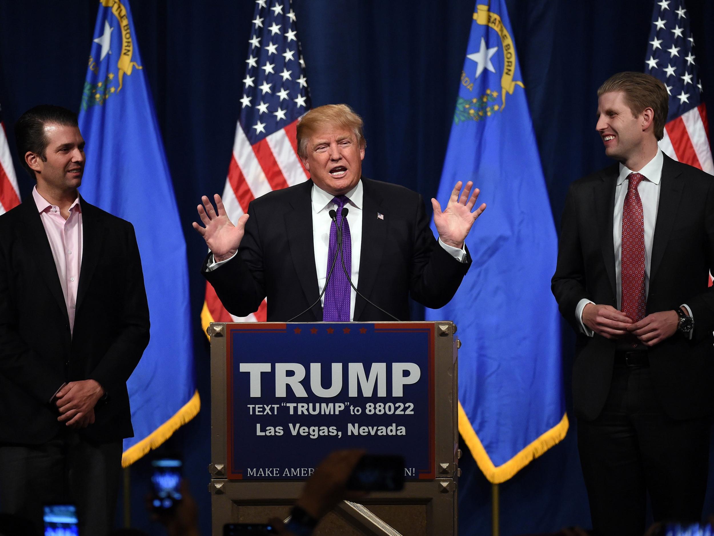 Trump speaks as his sons Donald Trump Jr. (L) and Eric Trump (R) look on during a caucus night watch party