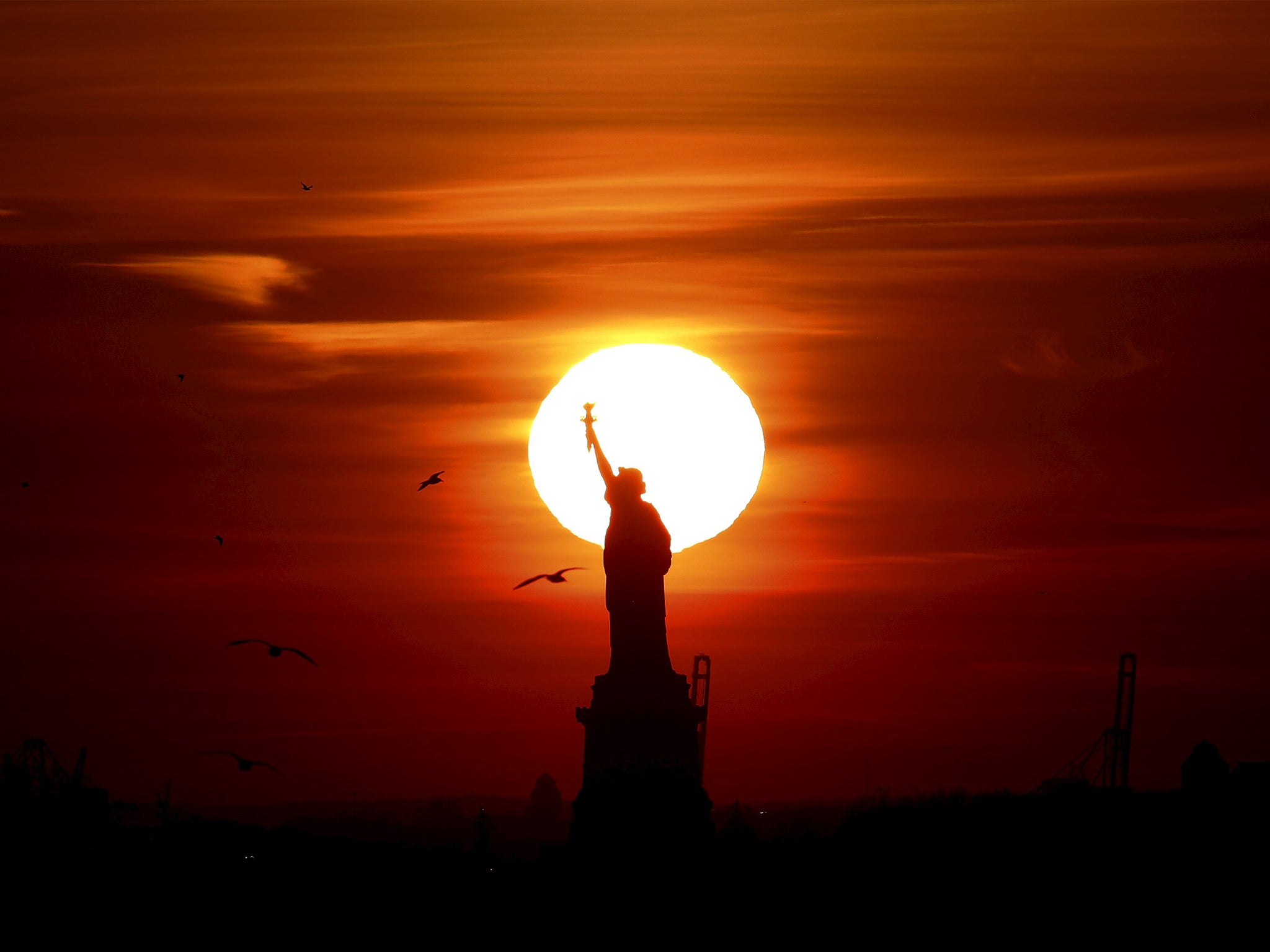 The sun sets behind the Statue of Liberty in New York's Harbor as seen from the Brooklyn borough of New York