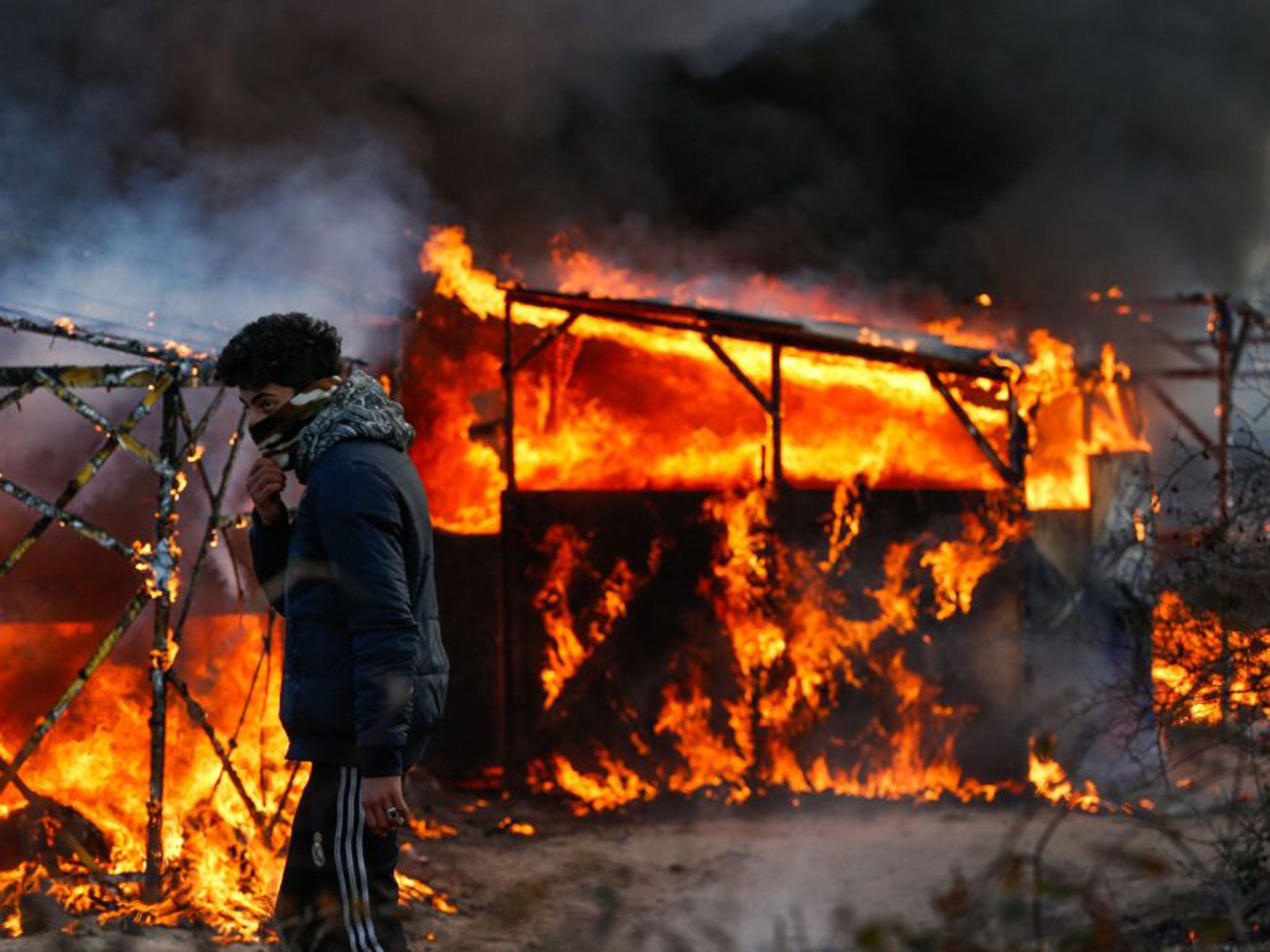 A refugee watches a shelter burn during the start of the expulsion at the Jungle camp